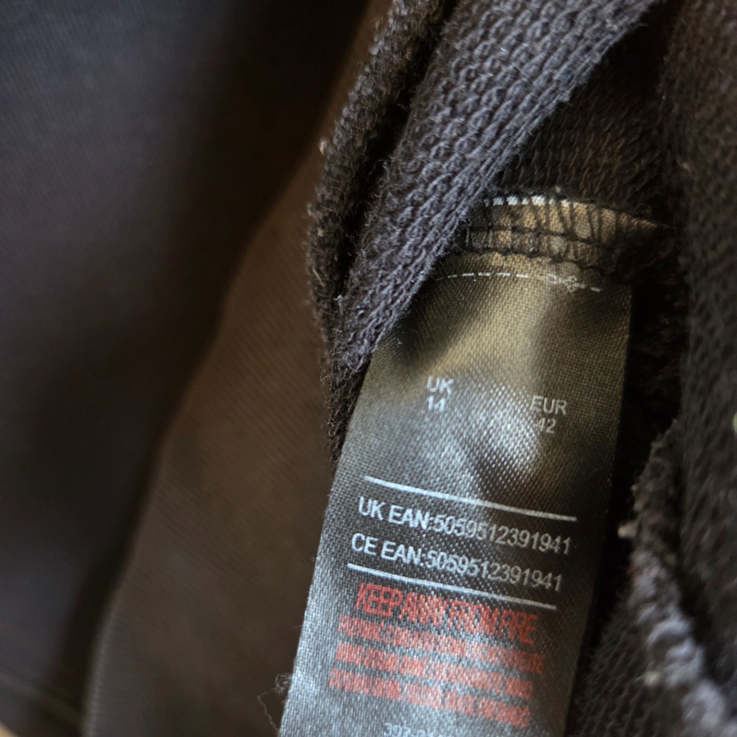 Close-up of a black clothing tag on an upcycled The Rolling Stones breastfeeding & pumping leopard band sweatshirt (UK14, EU42, 100411) with product codes and a red warning: KEEP AWAY FROM FIRE.