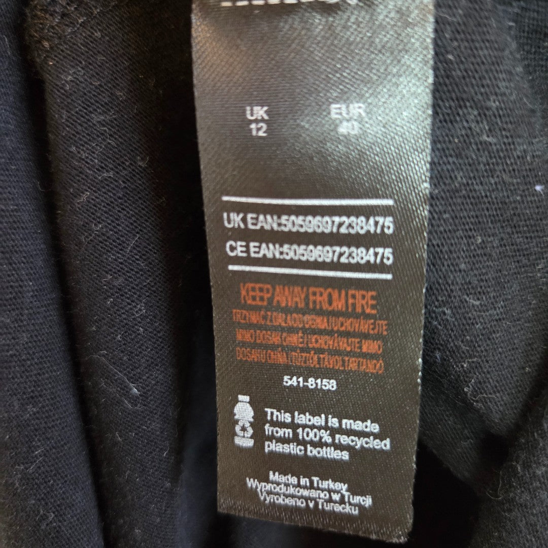 The KISS Upcycled Breastfeeding & Pumping Black Band t-shirt dress UK12 has a black label with UK/EU barcodes, an orange KEEP AWAY FROM FIRE warning, 100% recycled plastic bottles note, and Made in Turkey—ideal for eco nursing wear.
