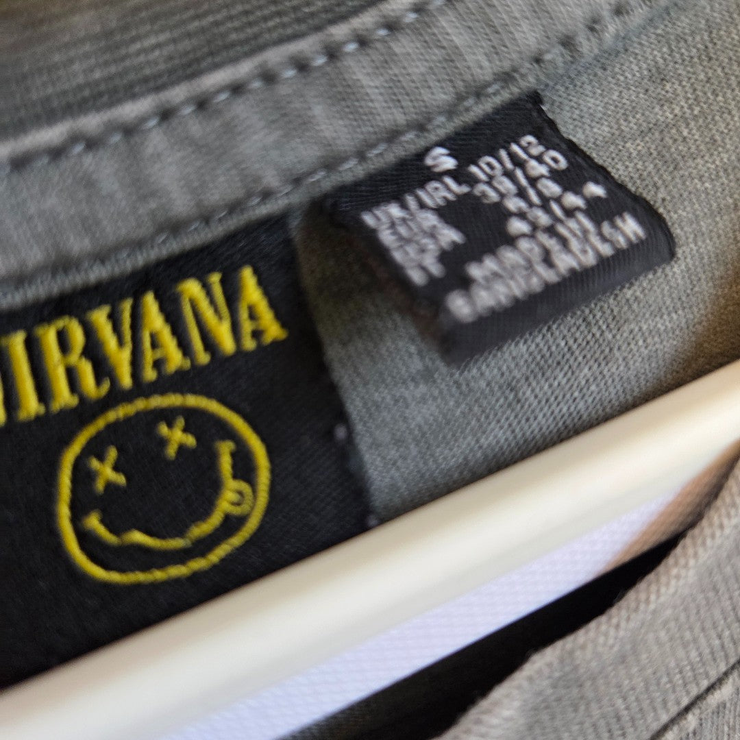 Close-up of an affordable grey/pink Nirvana band T-shirt dress by Primark (S/UK10-12), featuring the yellow logo and smiley face, plus size and care label, all hanging on a white plastic hanger. Product: Upcycled Nursing & Pumping Dress.