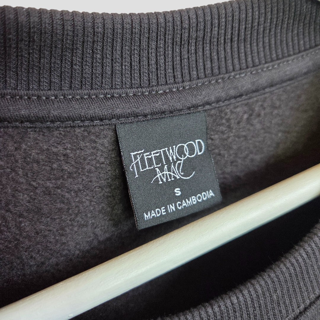A close-up shows a black Primark label on a gray Upcycled Breastfeeding & Pumping Fleetwood Mac Band Sweatshirt (S, 100433), made in Cambodia. A wooden hanger sits beneath the collar—an affordable, stylish choice for nursing moms.