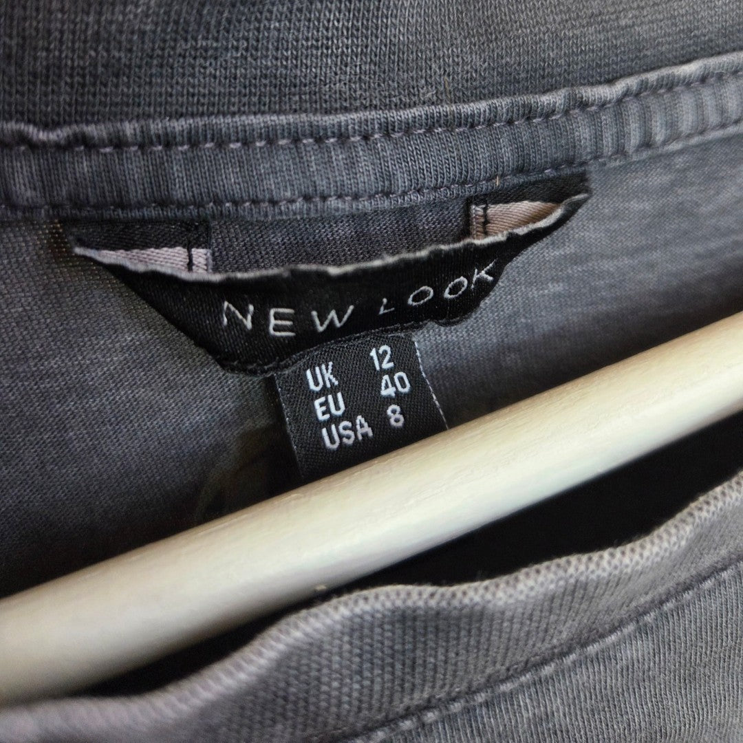 A close-up of a black New Look label on a gray Upcycled Breastfeeding & Pumping Bowie Band t-shirt (UK 12, EU 40, USA 8), displayed on a white wooden hanger.