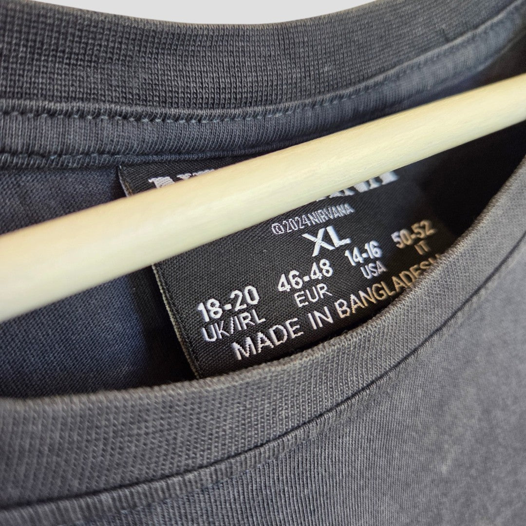 Close-up of a black Primark label inside an XL (UK18/20) Upcycled Breastfeeding & Pumping Grey/Turquoise Nirvana Angel Band t-shirt, with "Made in Bangladesh" text and a wooden hanger visible above.