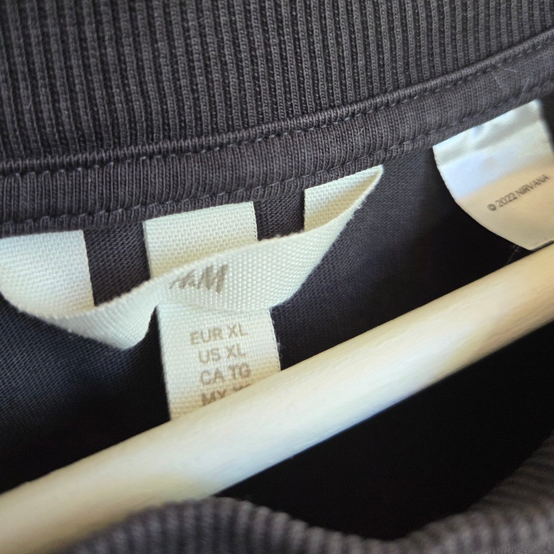Close-up of a black H&M Upcycled Breastfeeding & Pumping Nirvana Angel Band t-shirt (XL) on a wooden hanger, featuring size tags on a white label—ideal as stylish nursing clothing.