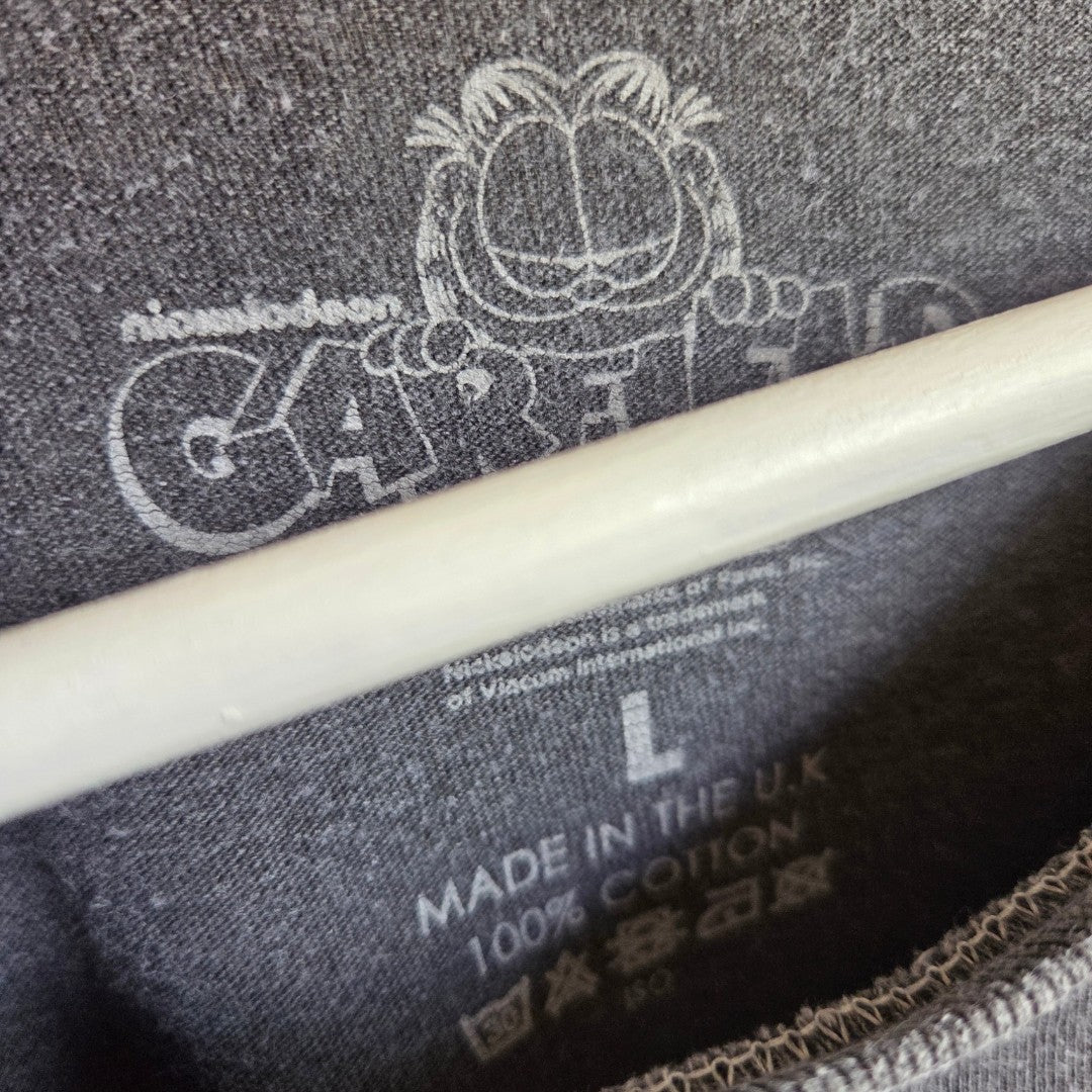 Close-up of a grey label inside the Garfield Upcycled Breastfeeding & Pumping Mood t-shirt (L), showing an outline of Garfield above "GARFIELD" and "MADE IN THE U.K.", plus 100% COTTON, size L, and care symbols.