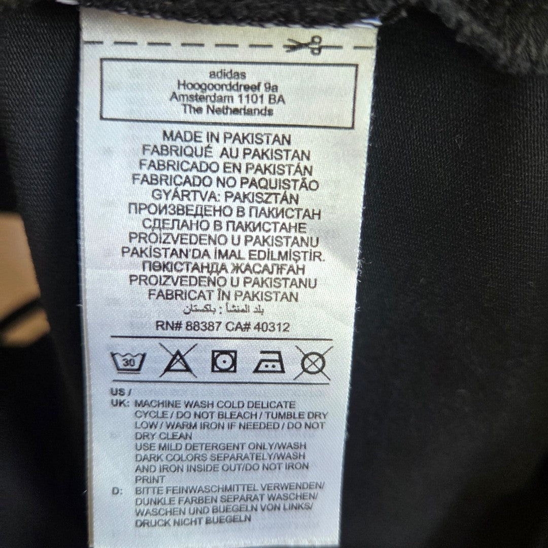 An Adidas XXL (UK24/26) Upcycled Breastfeeding & Pumping Black/White Logo t-shirt label lists care symbols: machine wash cold, do not bleach, tumble dry low, do not iron, plus washing instructions in several languages and Made in Pakistan.