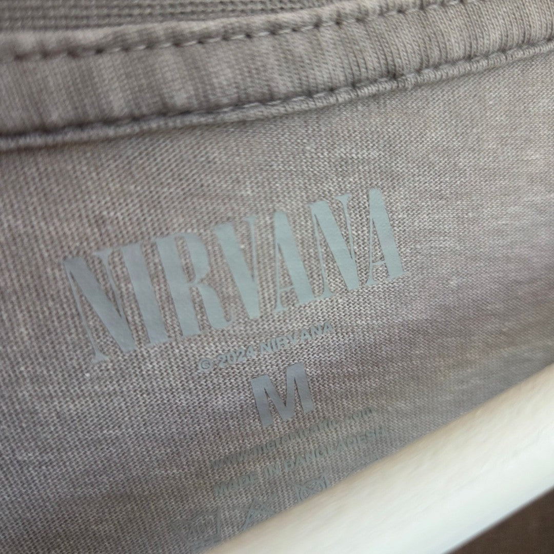 Close-up of a gray Primark shirt label with "NIRVANA" in bold above sizing info, showing it's a medium (UK12/14) Upcycled Breastfeeding & Pumping Grey/Pink Nirvana Angel Band t-shirt.