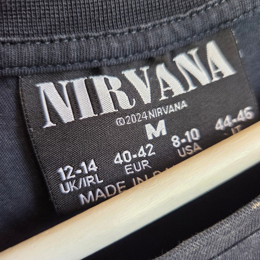 Close-up of a black label inside a Primark Upcycled Breastfeeding & Pumping Nirvana Turquoise Angel Band t-shirt (M, UK12/14), showing band name, size info, and conversions—perfect for stylish nursing moms. "Made in" is partly visible.