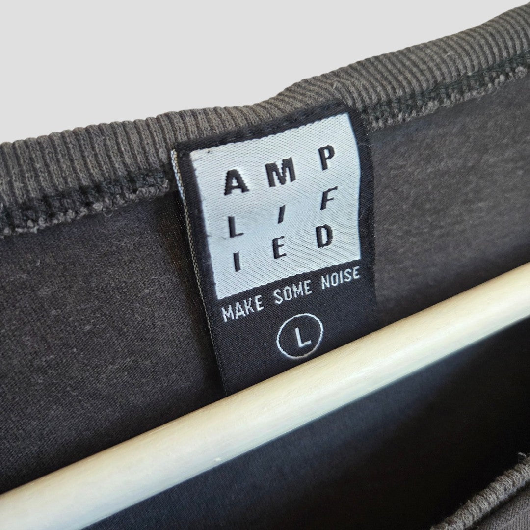 Close-up of a black clothing label inside a dark garment. The label reads AMPLIFIED with MAKE SOME NOISE below it, and an L size indicator at the bottom. This Upcycled Breastfeeding (Nursing) & Pumping Grey 1975 Led Zeppelin Band t-shirt (L, 100562) by Amplified is crafted from eco-friendly materials, designed for those who value both style and sustainability. A wooden hanger is visible underneath.