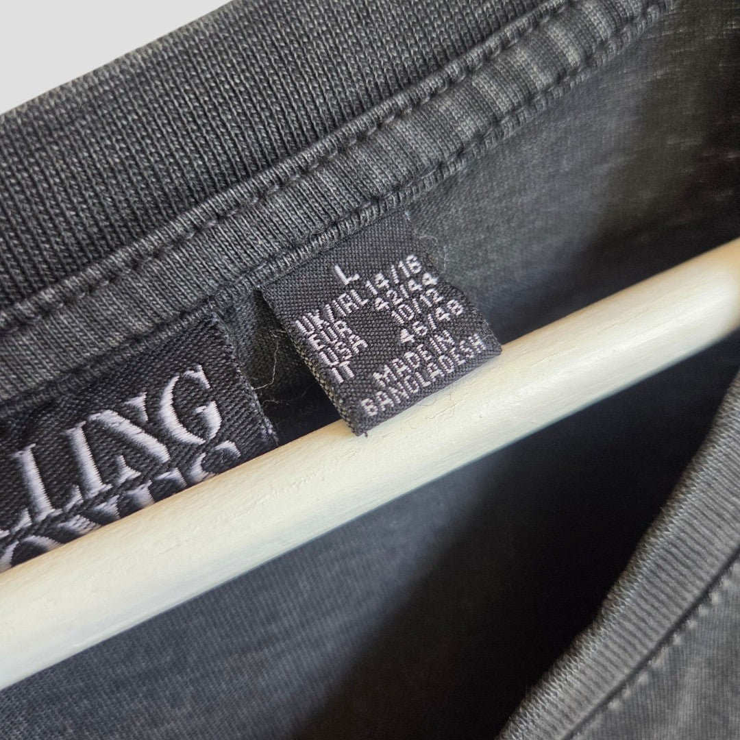 Close-up of a black Primark clothing tag on the affordable Upcycled Breastfeeding (Nursing) & Pumping The Rolling Stones Oversized Band t-shirt dress (L/UK14/16), displaying size details for various regions and "Made in Bangladesh" in white text. A wooden hanger is also visible.
