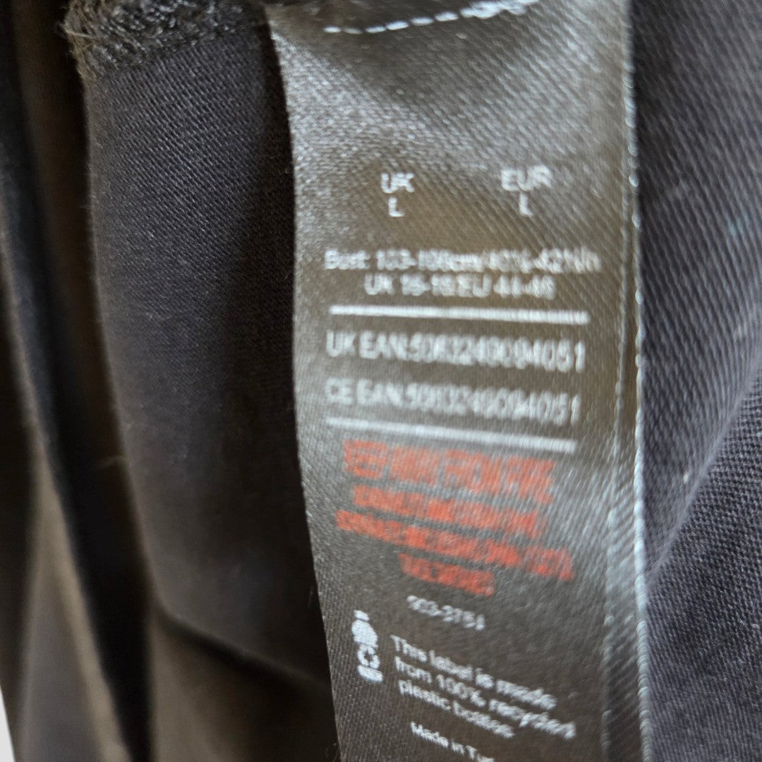 A close-up of a black clothing tag on the Def Leppard Upcycled Breastfeeding (Nursing) & Pumping Snow Band t-shirt (size L, product code 100544) shows partially visible UK and EUR size details, care instructions, and barcodes. Some text is blurred, but washing symbols can be seen—highlighting this item as part of an eco-friendly nursing collection.