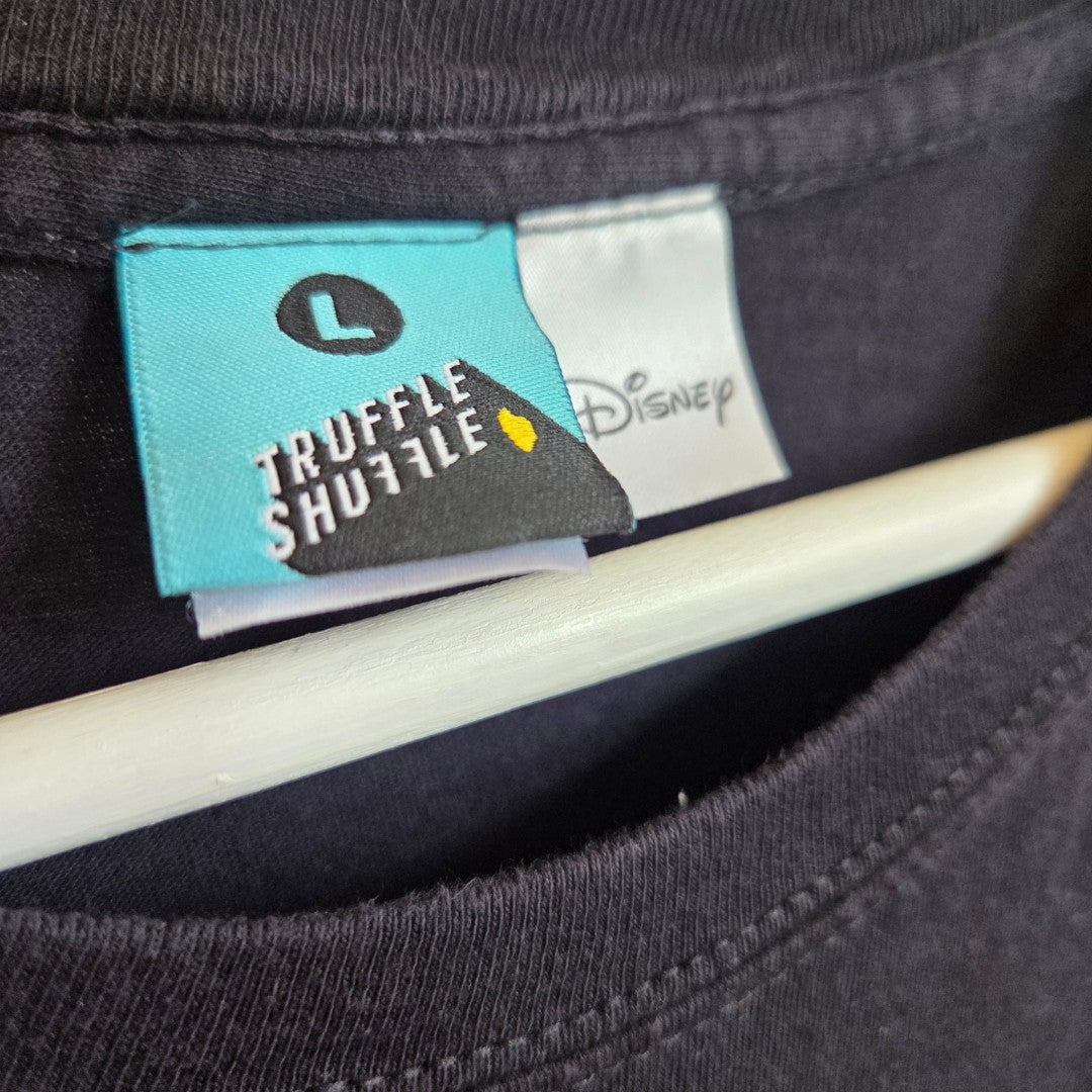 A close-up of a clothing tag on a black Upcycled Breastfeeding & Pumping The Nightmare Before Christmas t-shirt (size L) by Truffle Shuffle, featuring Disney branding and a small yellow detail—all hanging on a white hanger—captures the playful yet practical essence of affordable nursing wear designed for breastfeeding and pumping.