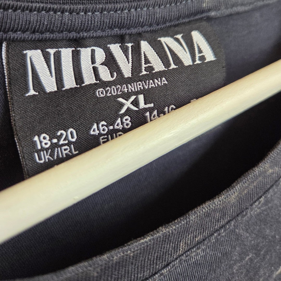 Close-up of a black t-shirt collar featuring a label that reads NIRVANA along with size details: XL, UK/IRL 18-20, EU 46-48, FR 44-46. The label displays ©2024 NIRVANA and the hanger is visible. This Upcycled Breastfeeding (Nursing) & Pumping Grey Nirvana Turquoise Angel Oversized Band t-shirt XL (UK18/20) by Primark offers stylish comfort and an affordable option for those seeking nursing clothes or breastfeeding-friendly fashion with a focus on fit.
