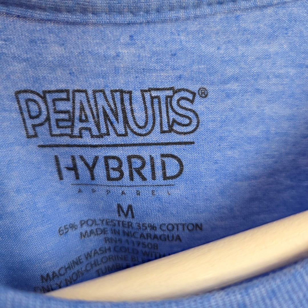 Close-up of the inner label on a blue Peanuts Upcycled Breastfeeding (Nursing) & Pumping Snoopy t-shirt in size M (100605), displaying brand, material details, and care instructions. This eco-friendly and affordable design offers both comfort and style. The bottom of the image features part of a wooden hanger.