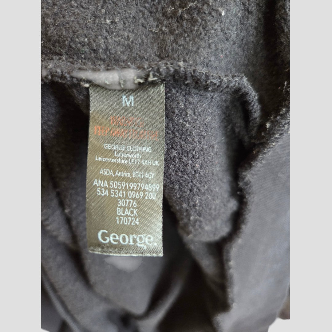 Close-up of a black clothing tag inside the Upcycled Breastfeeding (Nursing) & Pumping Black/White Fleetwood Mac Band Sweatshirt M (100576). The tag displays care instructions, size M, brand name George, and product codes in white text on a black background. This unique sweatshirt is an affordable nursing garment with practical details designed for comfort.