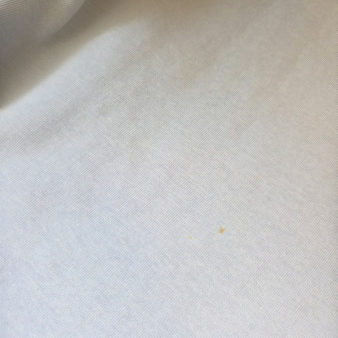 A close-up of white fabric from the George Upcycled Breastfeeding & Pumping Blue Floral Paradise Lightweight Sweatshirt (XL, UK20/22) shows a small, faint yellowish stain visible near the center-right area.
