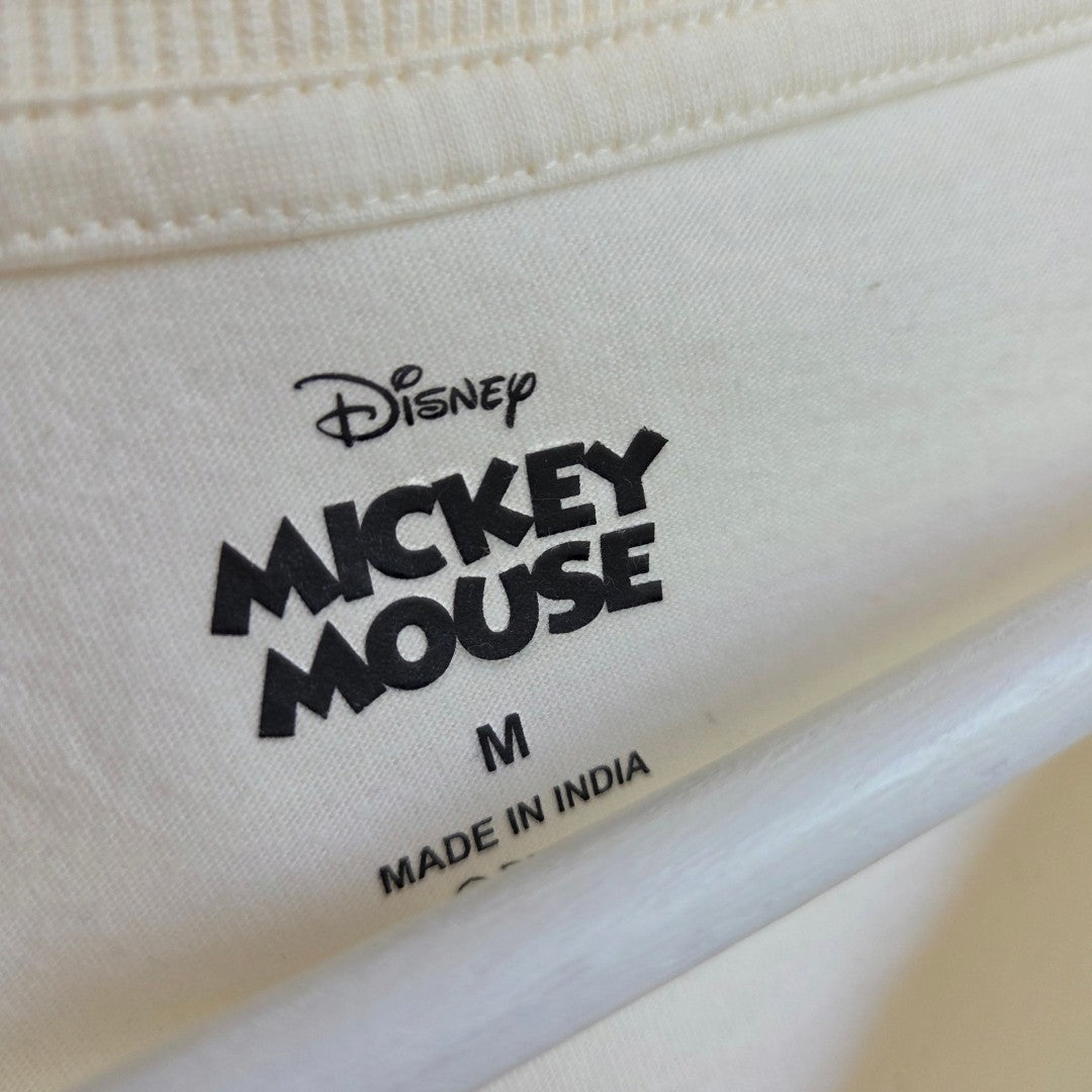 Close-up of a clothing tag on a white Upcycled Breastfeeding (Nursing) & Pumping Cream/Orange Mickey Mouse t-shirt M (100636), featuring the Disney logo, the words Mickey Mouse, a size M, and Made in India.