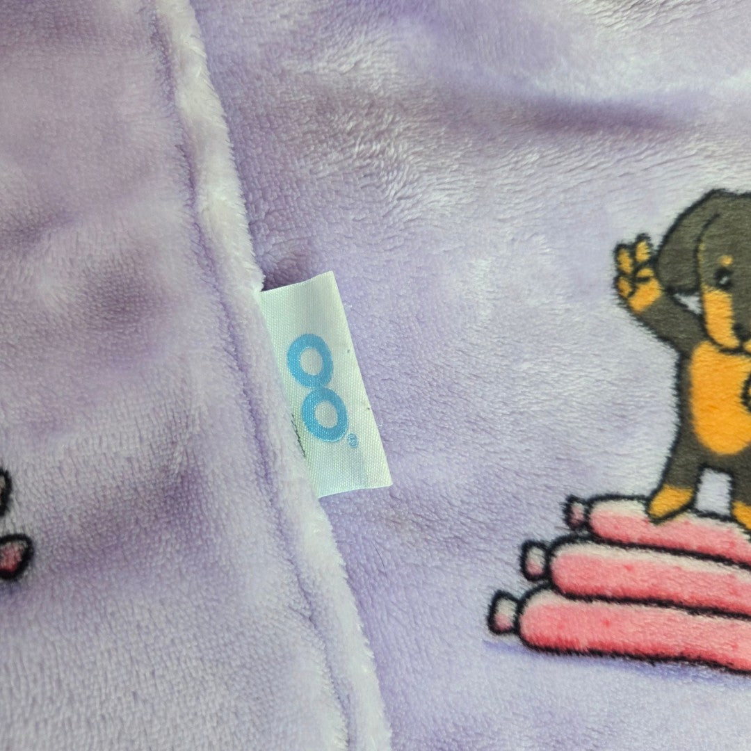 Close-up of a soft purple Upcycled Breastfeeding (Nursing) & Pumping Purple Dachshund Oodie hoodie XXL (100647) with a blue infinity logo tag, next to a cartoon dachshund standing on a stack of pink sausages.