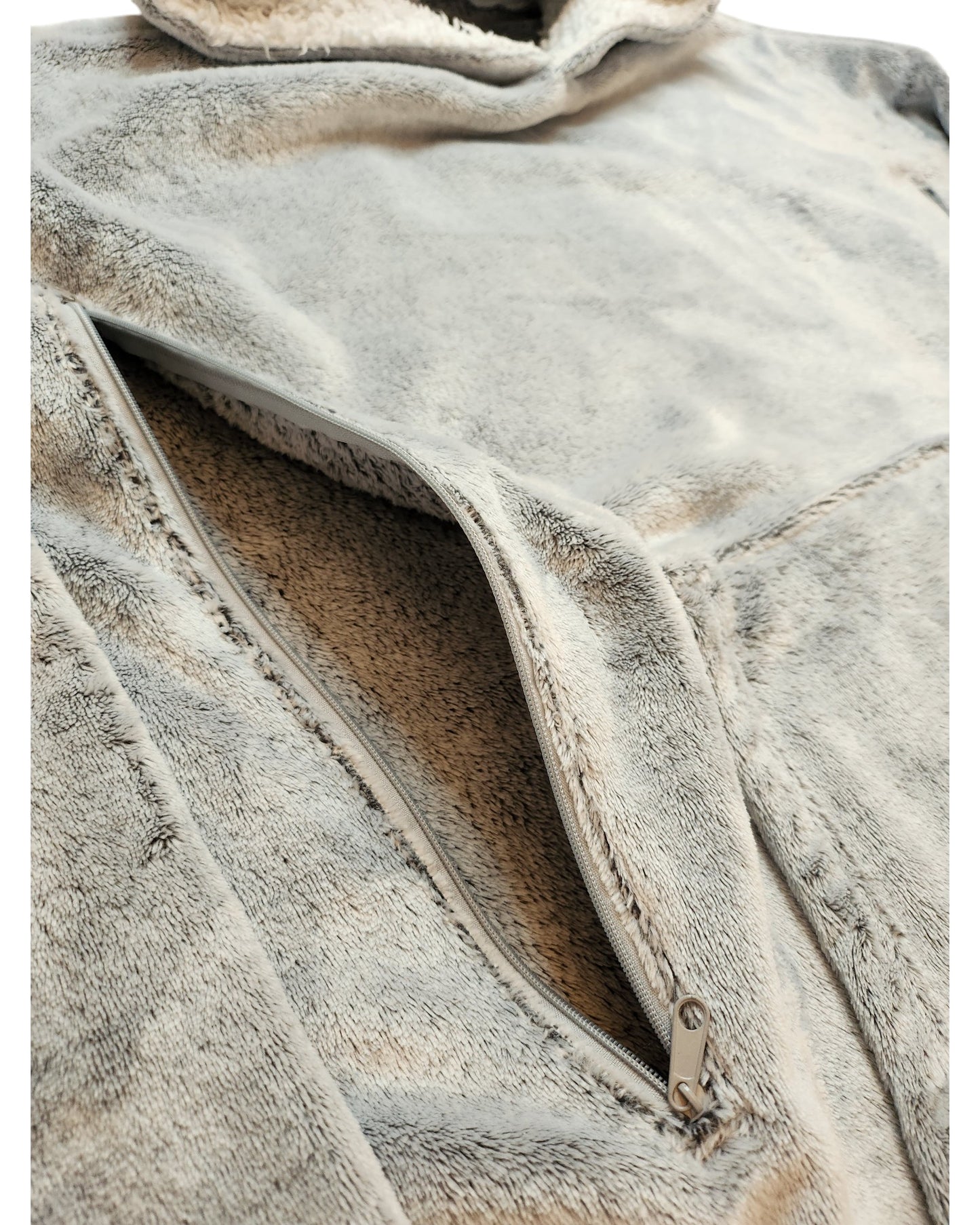 A close-up of the beige Upcycled Breastfeeding & Pumping Blanket Hoodie L by touched out mama shows a partially open diagonal zipper on the fluffy fleece front. Its soft fabric exudes warmth and comfort, while the preloved metallic zipper adds a charming reflective touch.