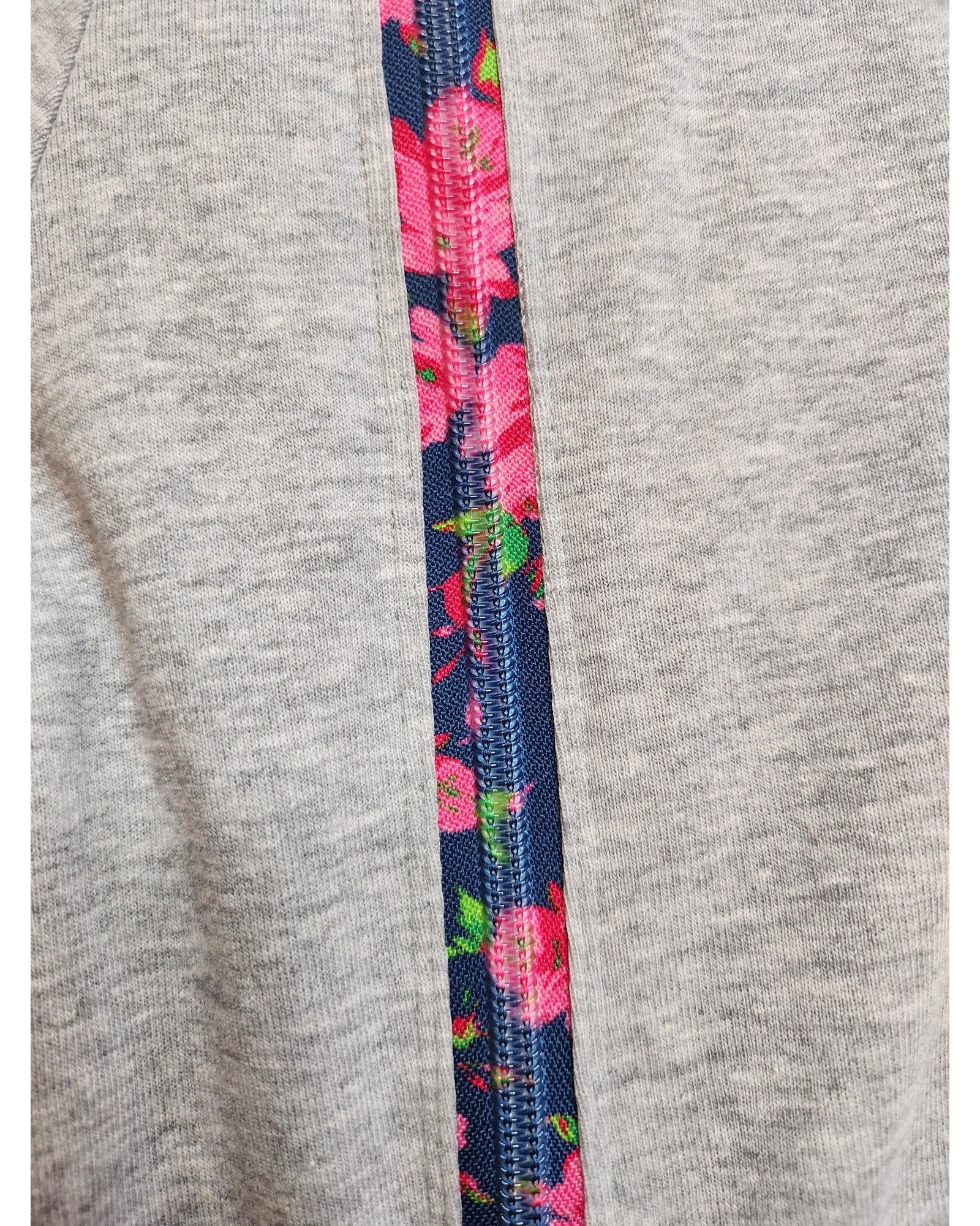 Close-up of the touched out mama Upcycled Breastfeeding & Pumping Grey Floral Zip t-shirt features a vertical zipper for easy nursing; the inner side reveals a vibrant blue floral pattern with pink flowers and green leaves, offering a stylish contrast to its plain gray, preloved design.