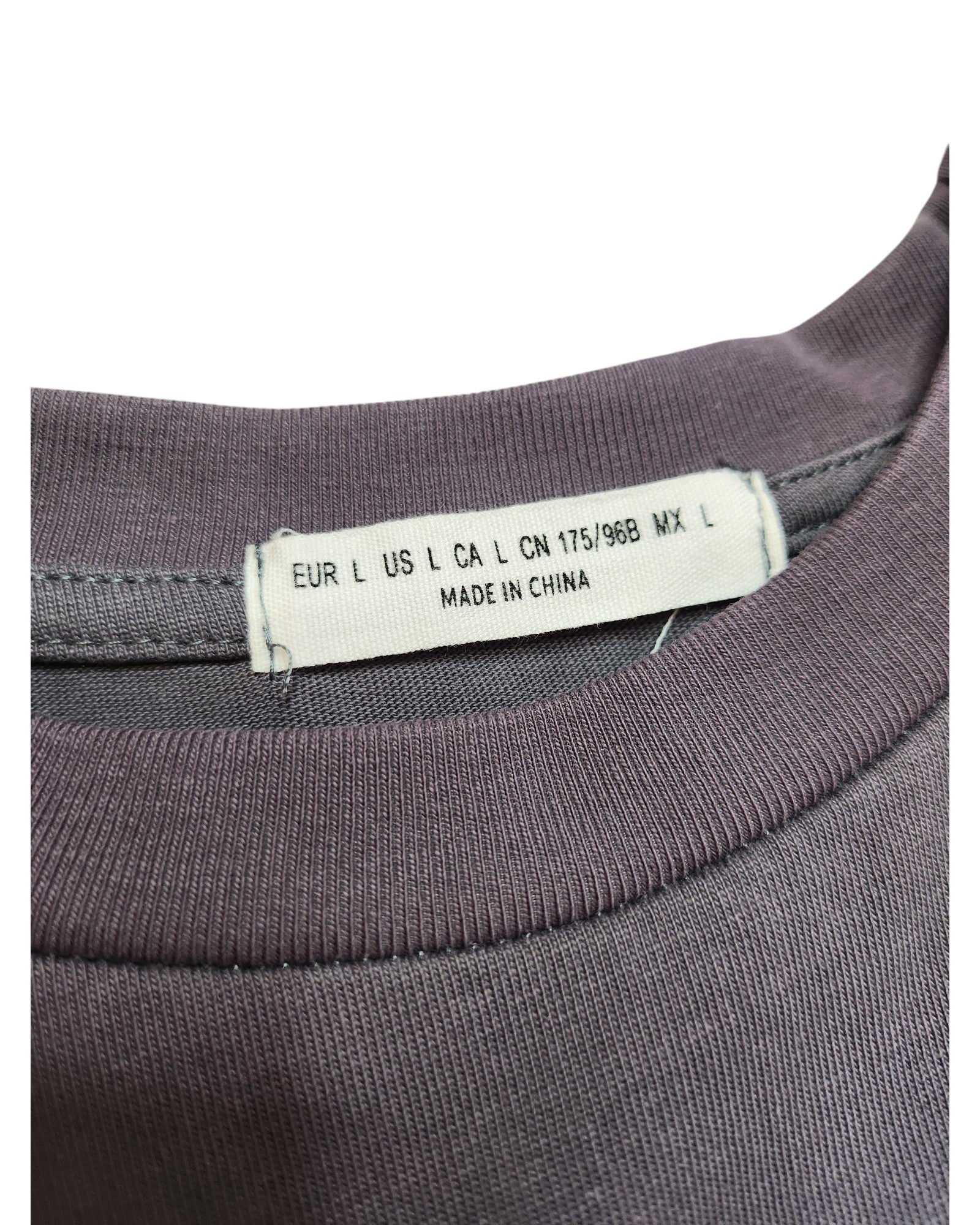 A close-up of the clothing tag on this preloved purple garment from touched out mama reveals size labels: EUR L, US L, CA L, CN 175/96B, MX L. It also reads Made in China, sewn neatly into the neckline of the Upcycled Breastfeeding & Pumping White Fox t-shirt.