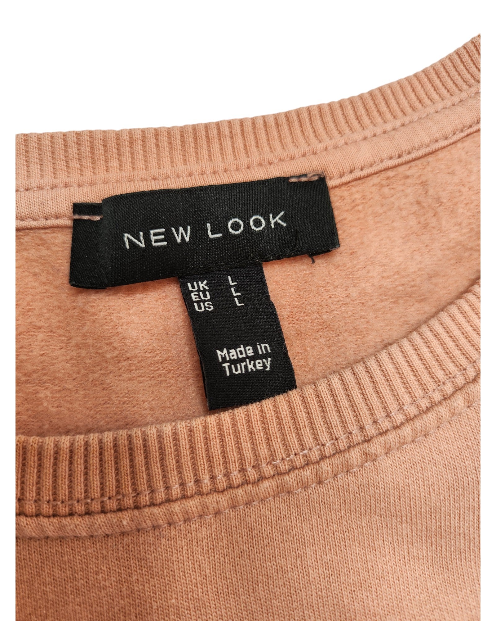Close-up of a beige Self Love Club sweatshirt with a ribbed neckline from touched out mama’s eco-friendly line. A label shows New Look and size UK/US/EU L in black on white. Another tag reads Made in Turkey, highlighting sustainability and function for breastfeeding or pumping.