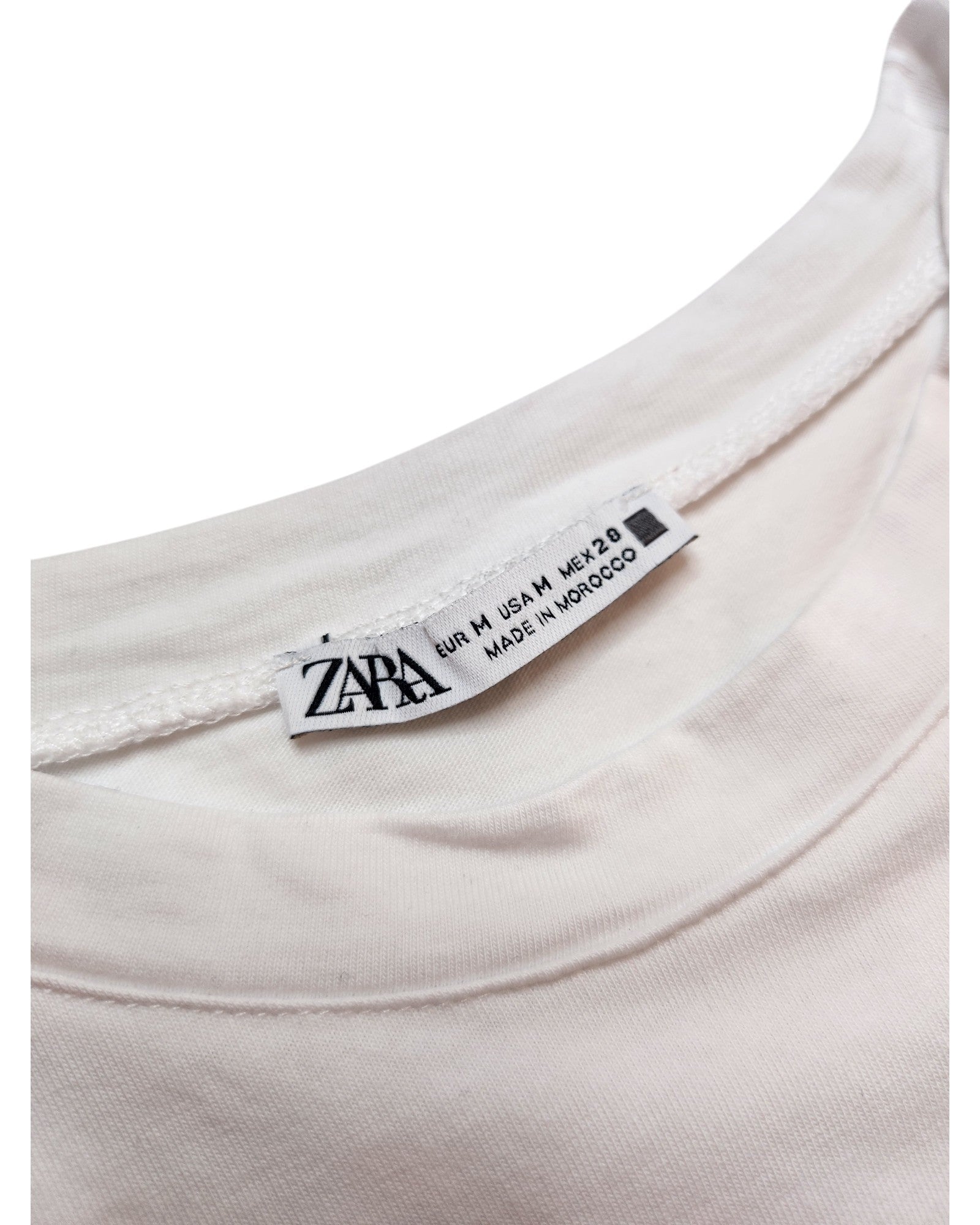 The label of a white touched out mama t-shirt, an eco-friendly brand, shows EUR M / USA M / MEX 28 sizes. Crafted in Morocco and placed against a plain white backdrop, this Upcycled Breastfeeding & Pumping Silver Face shirt promotes sustainable style.