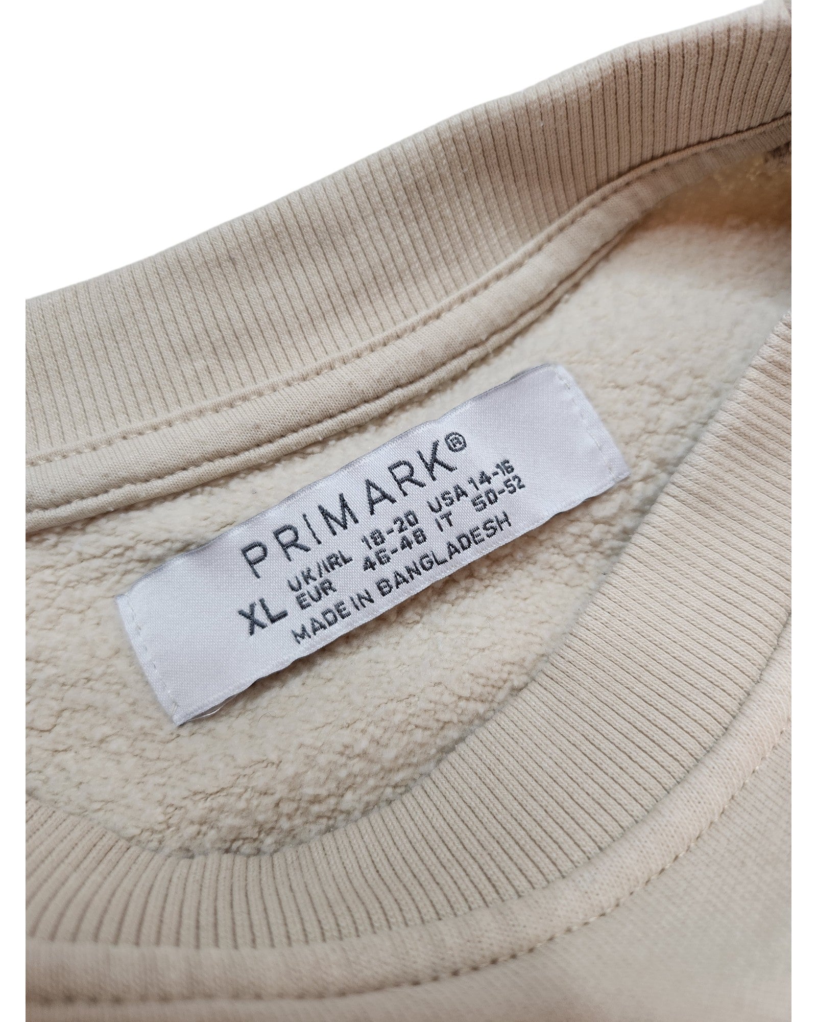 A close-up of a preloved label from touched out mamas innovative beige Upcycled Breastfeeding & Pumping The Kiss Sweatshirt XL reveals international size details, made in Bangladesh. The soft, fleece-like fabric enhances its appeal.
