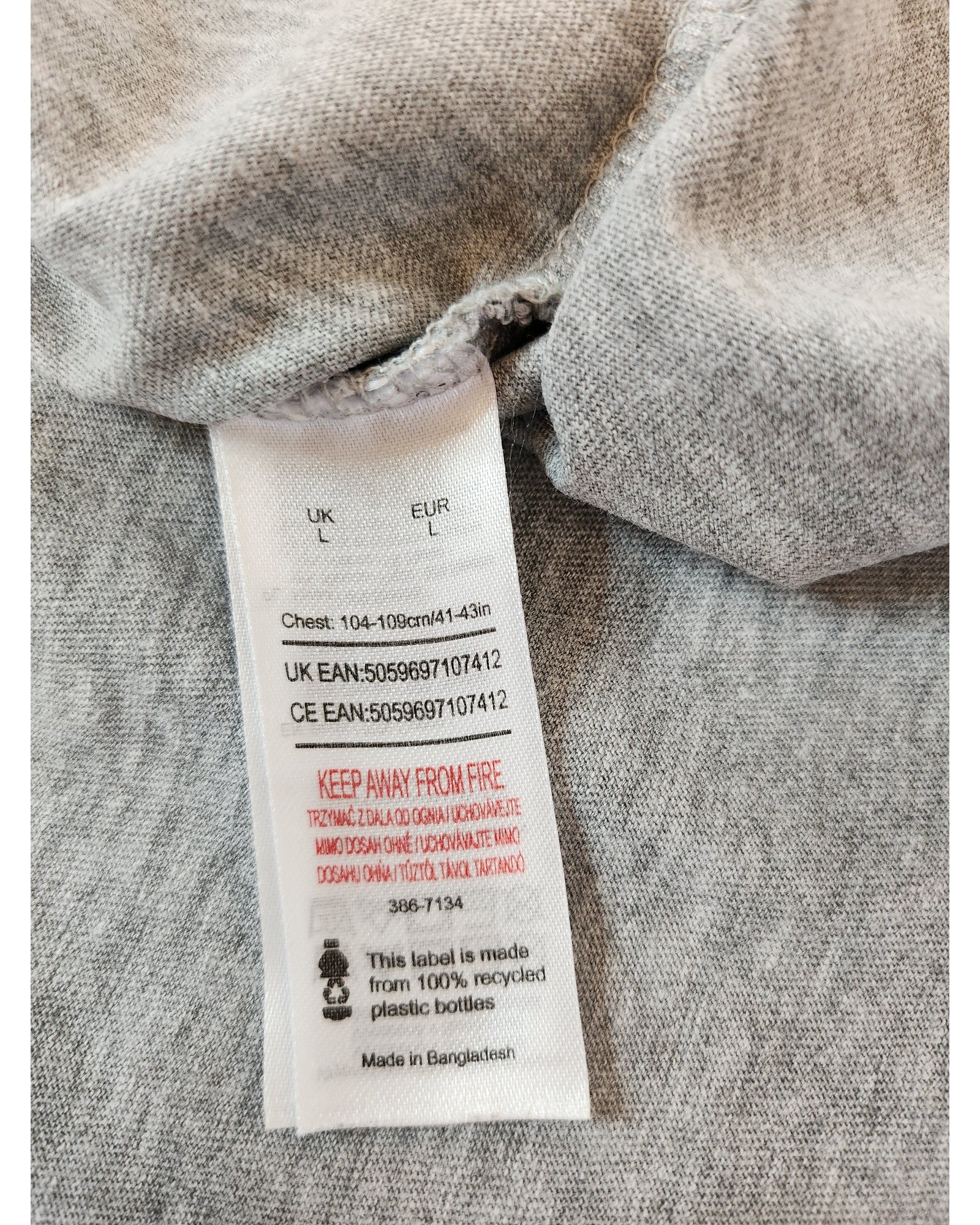 The touched out mama Upcycled Nursing & Pumping Rolling Stones Tie-dye T-shirt (size L) highlights its eco-friendly nature with a care label featuring UK and CE EAN codes and a fire safety warning. Made in Bangladesh from 100% recycled plastic bottles, this gray item is both stylish and sustainable.