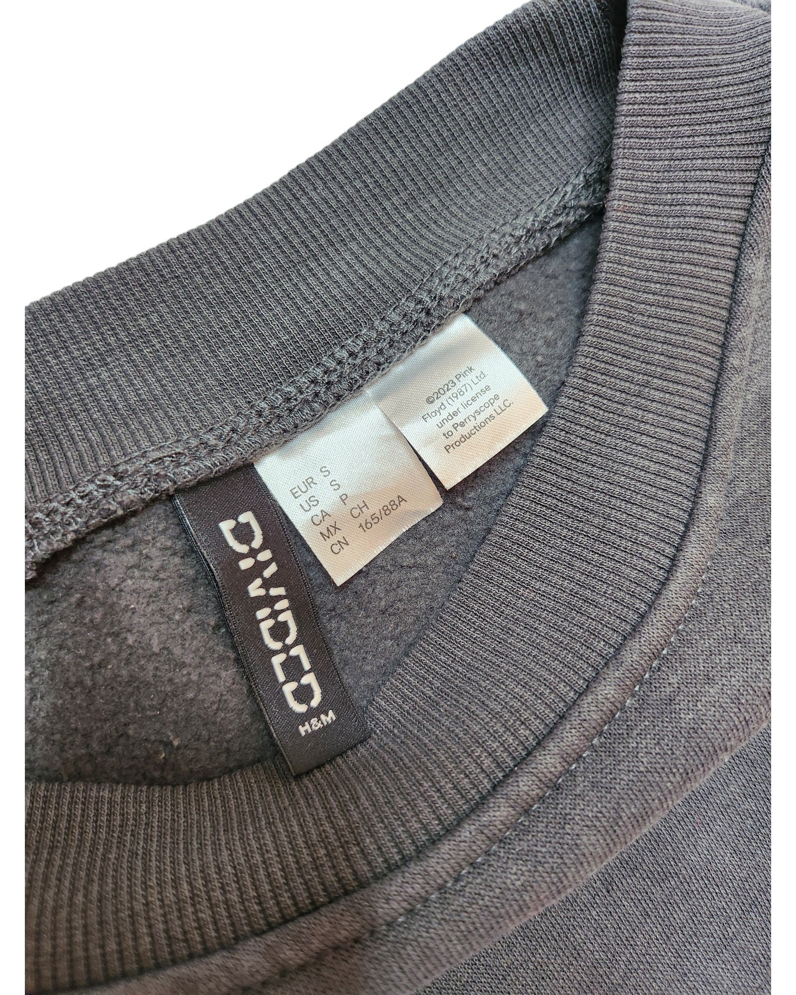 Close-up of the gray collar on a preloved Upcycled Breastfeeding & Pumping Pink Floyd Long-line Sweatshirt S by touched out mama, displaying EUR S and CH S size labels. The neatly crafted stitching highlights its unique fabric texture.