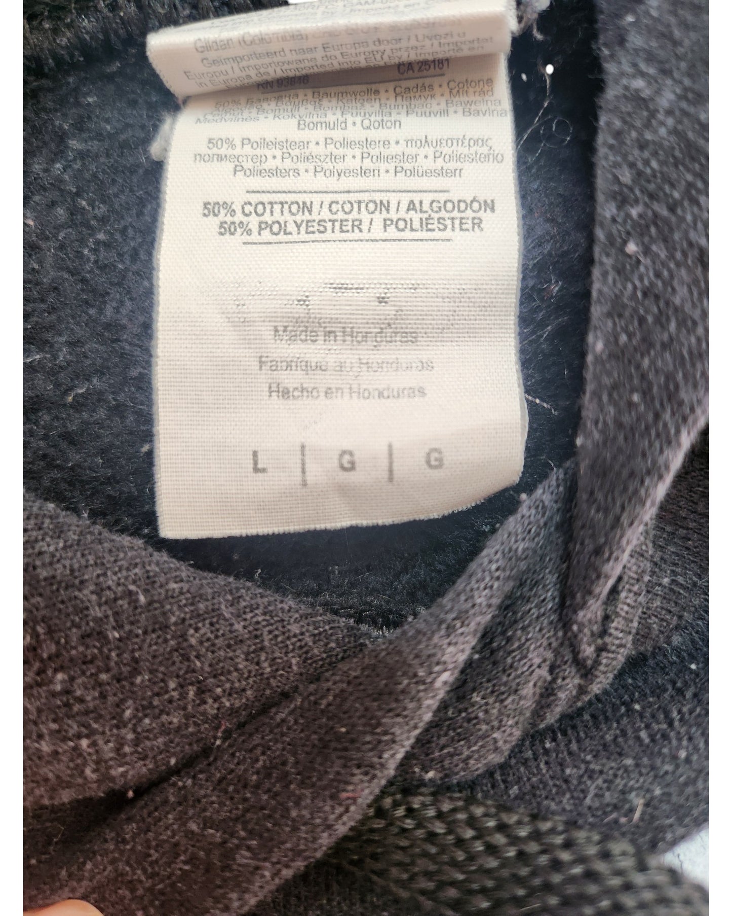Close-up of a touched out mama tag on eco-friendly apparel, displaying a 50% cotton and 50% polyester blend. Made in Honduras, it is size L/G/G. The surrounding dark fabric highlights the sustainable craftsmanship of the Upcycled Breastfeeding & Pumping Little Mix Hoodie L.