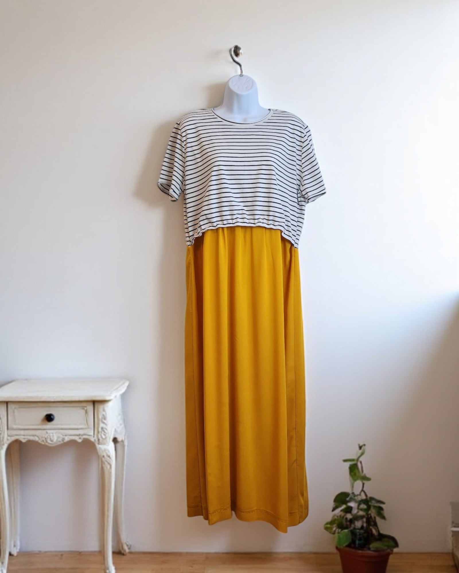 A mannequin showcases touched out mamas eco-friendly Upcycled Breastfeeding & Pumping Stripe Ochre Maxi Dress (M/L) beside a small white vintage table and a potted plant against a plain white wall.