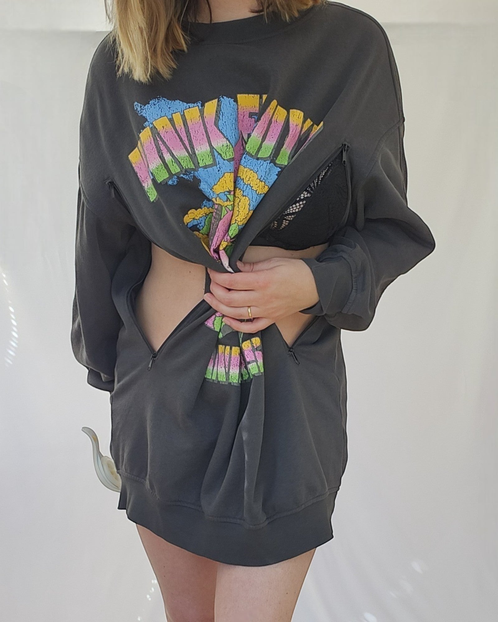 Wearing an H&M Upcycled Breastfeeding & Pumping Grey Pink Floyd Band Sweatshirt (L, 100440), a person unzips the sides and lifts the middle to reveal a black bra and part of their midsection; their face is not visible.