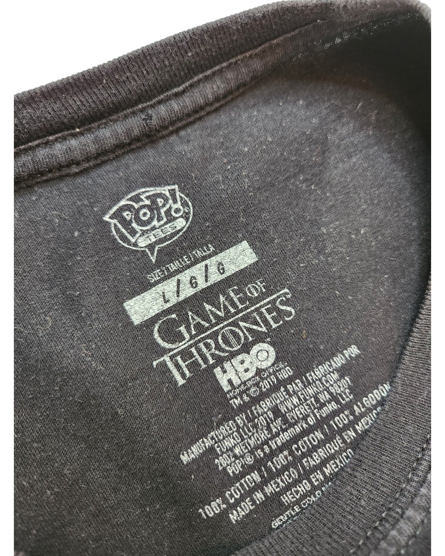Close-up of touched out mama’s Upcycled Breastfeeding & Pumping Game of Thrones t-shirt (size L) inner label, showing POP! VERO, handwritten number 11616, HBO branding, and care details in English and Spanish on this eco-friendly piece.