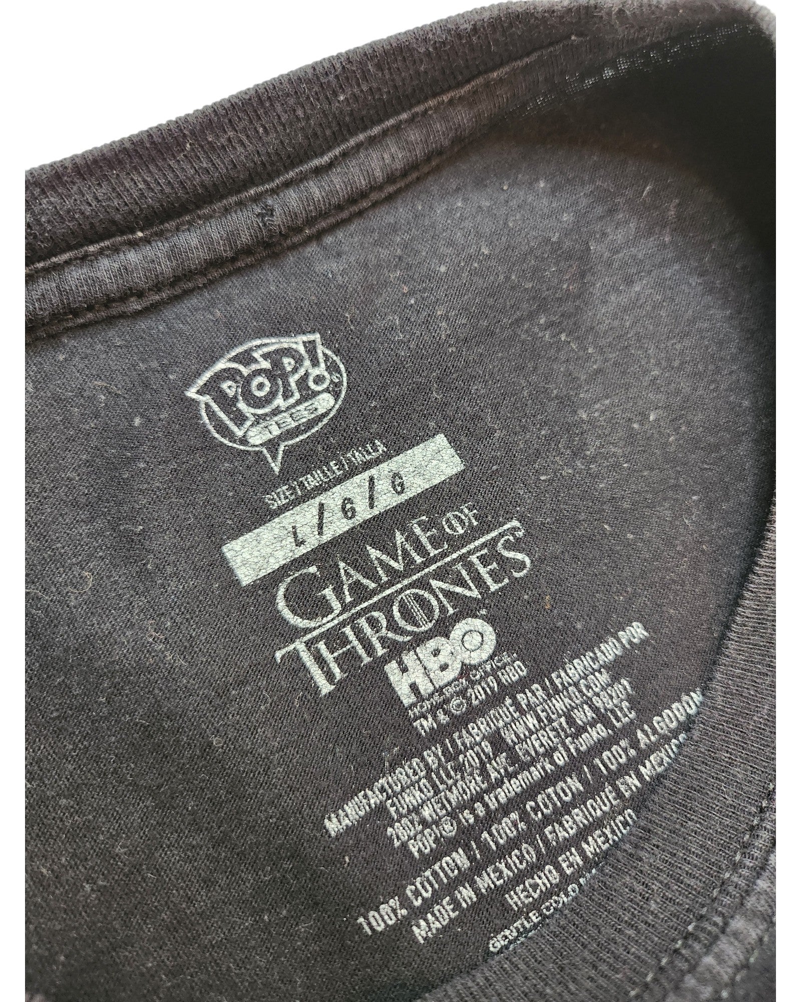 Close-up of touched out mama’s Upcycled Breastfeeding & Pumping Game of Thrones t-shirt (size L) inner label, showing POP! VERO, handwritten number 11616, HBO branding, and care details in English and Spanish on this eco-friendly piece.