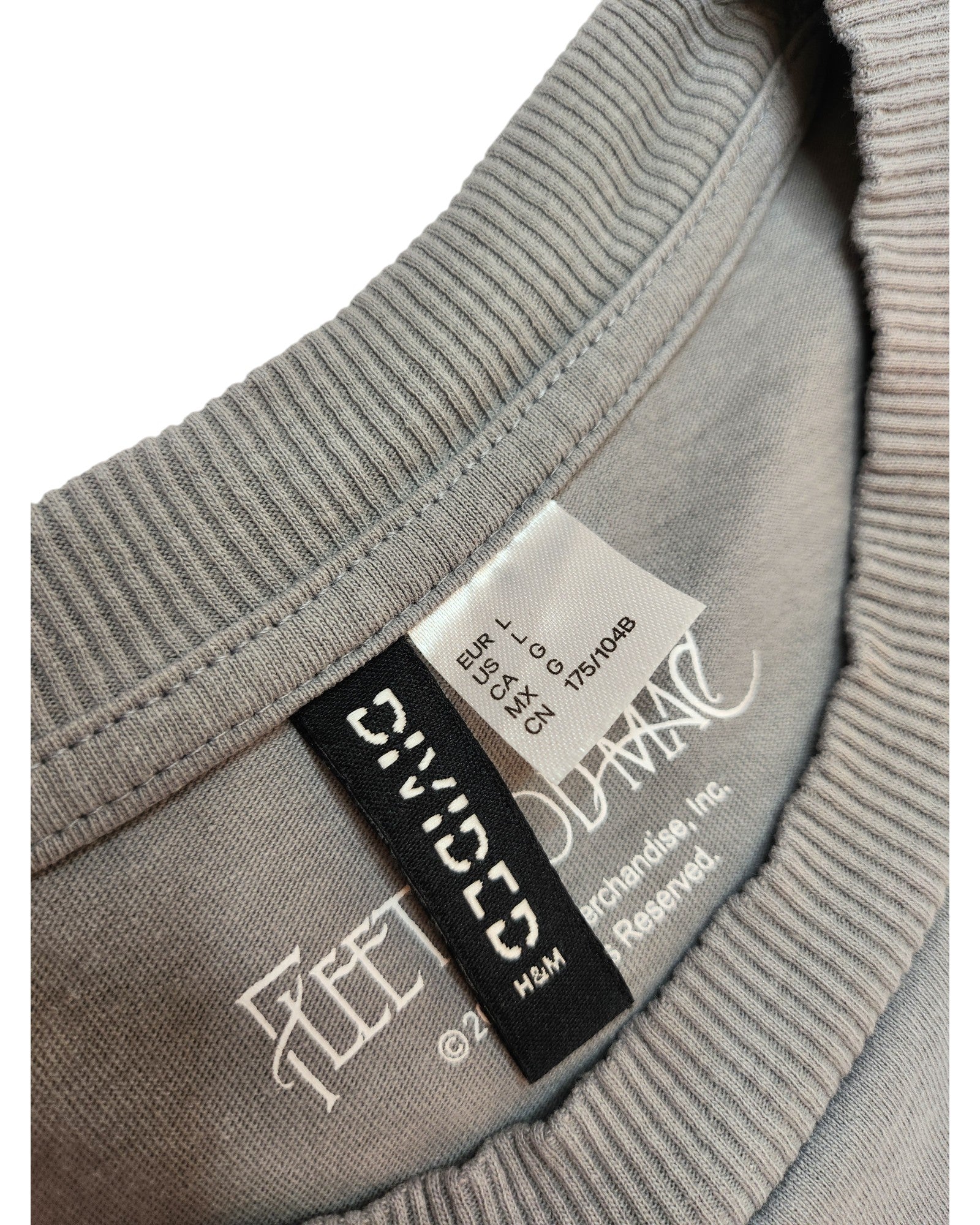 Close-up of a gray t-shirts collar, focusing on inner tags. The tags provide washing instructions and show size (EUR L, USA L, MEX G) with the brand touched out mama in a stylized font. This Upcycled Breastfeeding & Pumping Dreams Fleetwood Mac t-shirt highlights eco-friendly fashion principles.