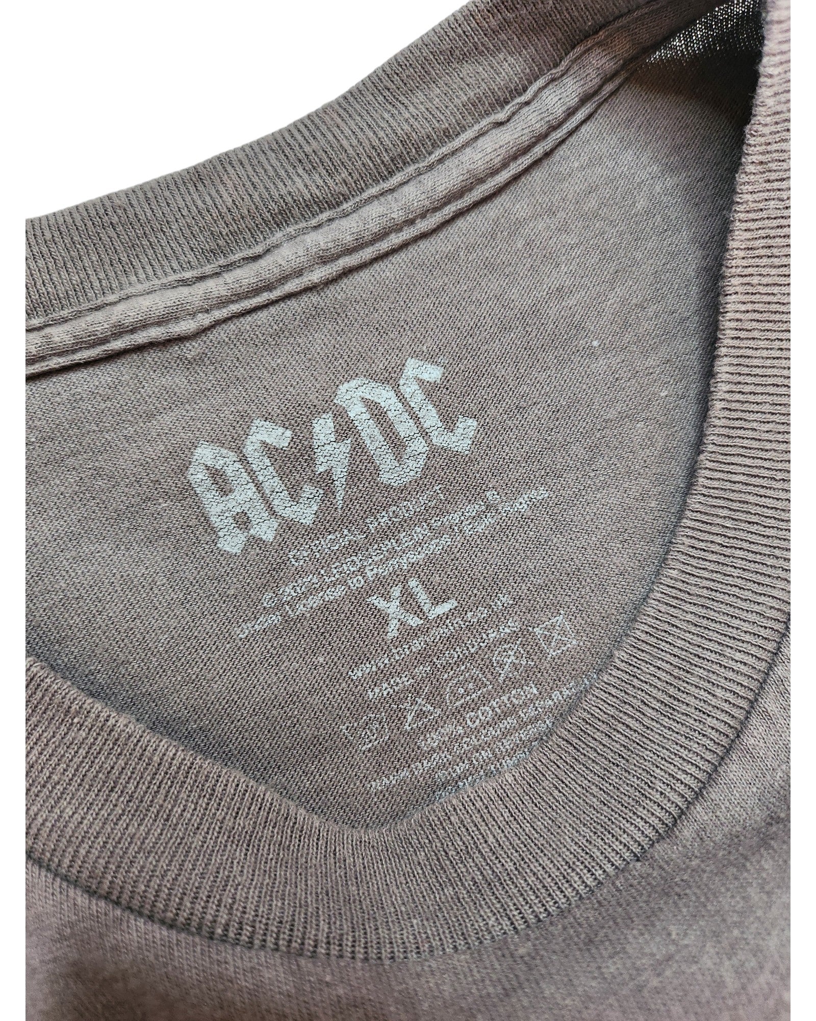 A close-up of a gray touched out mama T-shirt by AC/DC shows its preloved charm. The XL label includes washing instructions, and the soft fabric with ribbed edging hints at its past adventures, now upcycled for breastfeeding and pumping.