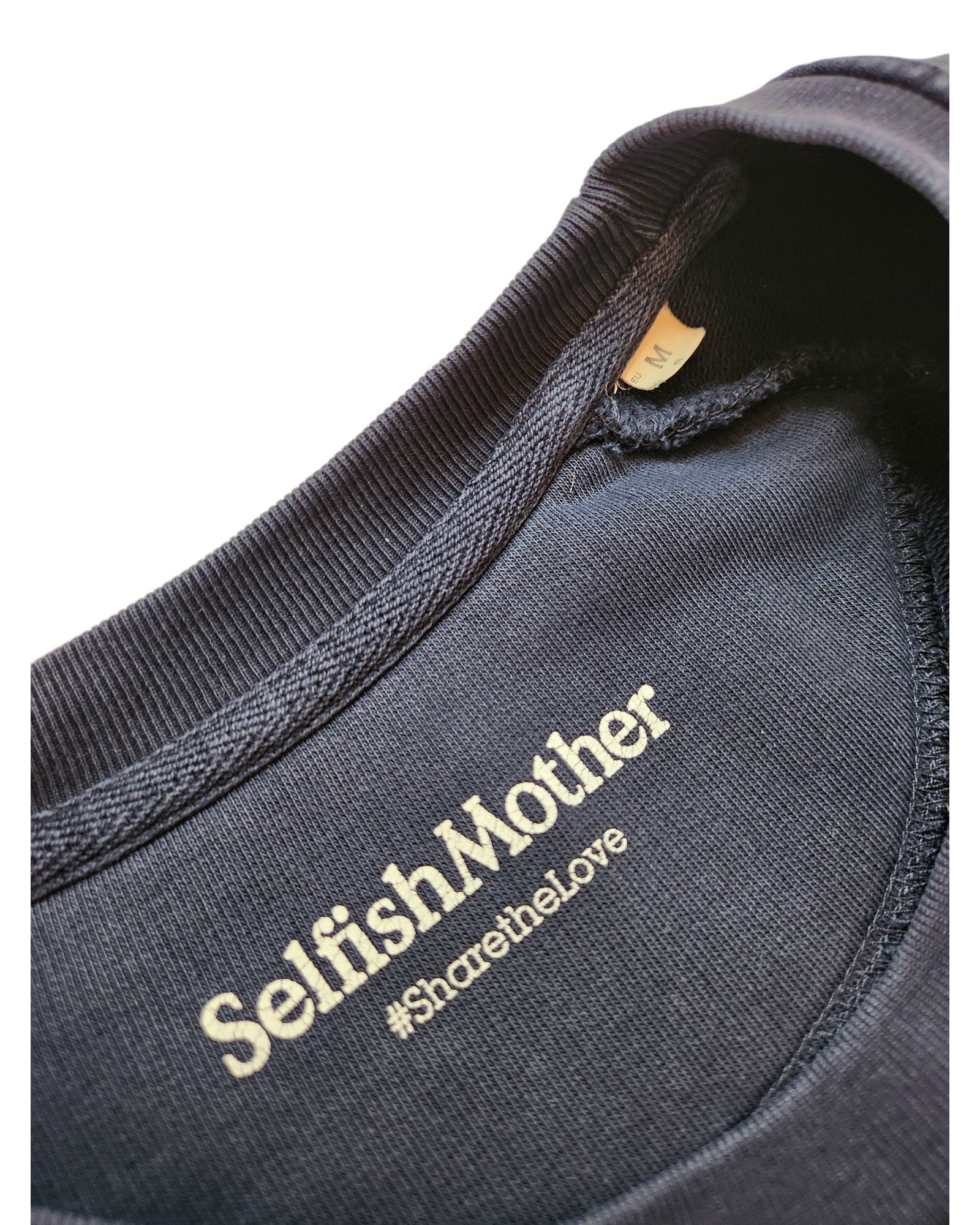 Close-up of a navy blue Upcycled Breastfeeding & Pumping Mother Sweatshirt (M) by touched out mama, featuring a white printed label and beige size tag inside the collar—an eco-friendly wardrobe choice.