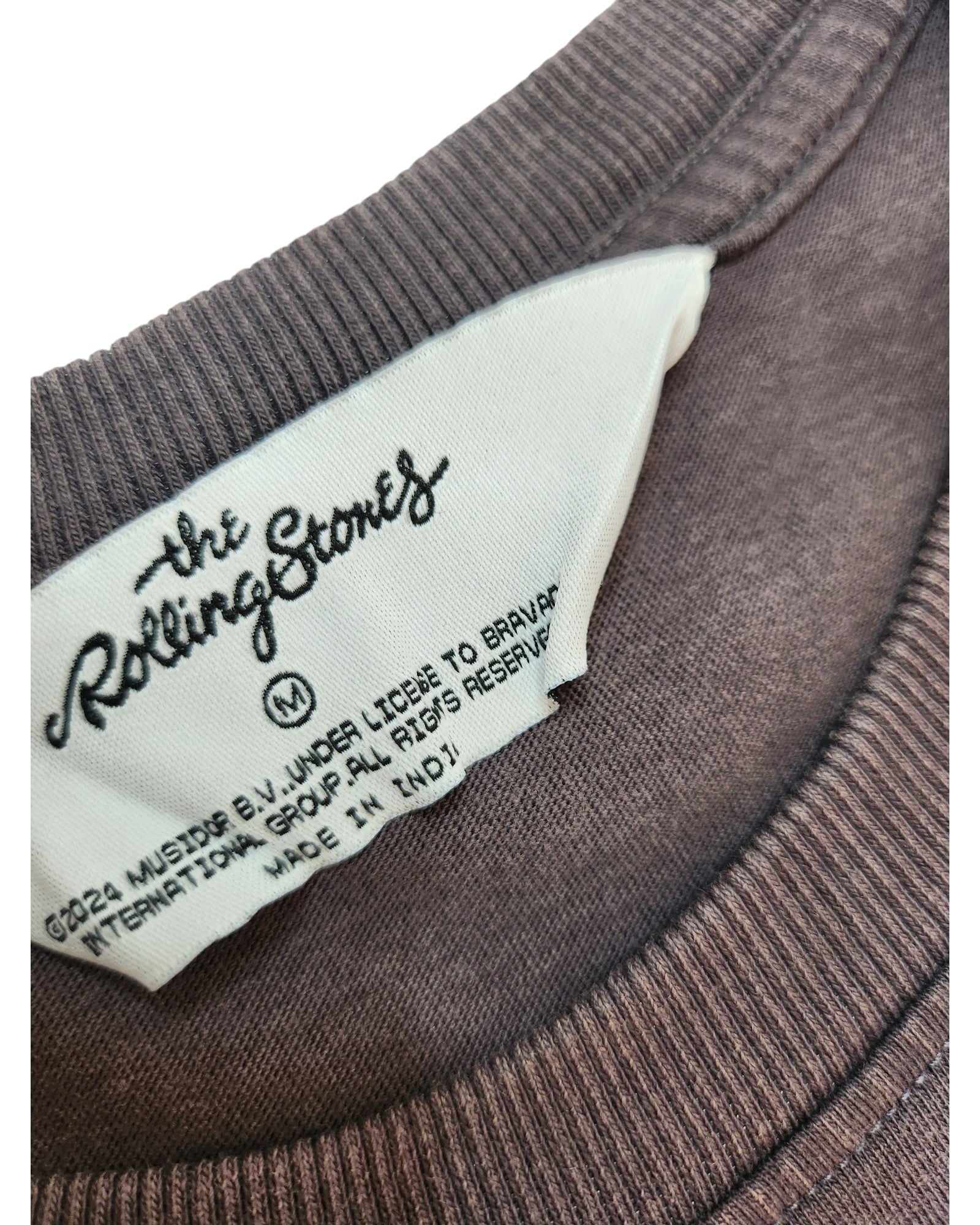 Close-up of a Primark clothing tag on an upcycled grey/white The Rolling Stones breastfeeding & pumping t-shirt, size M, made in India with licensing info—showcasing sustainable, eco-friendly fashion.