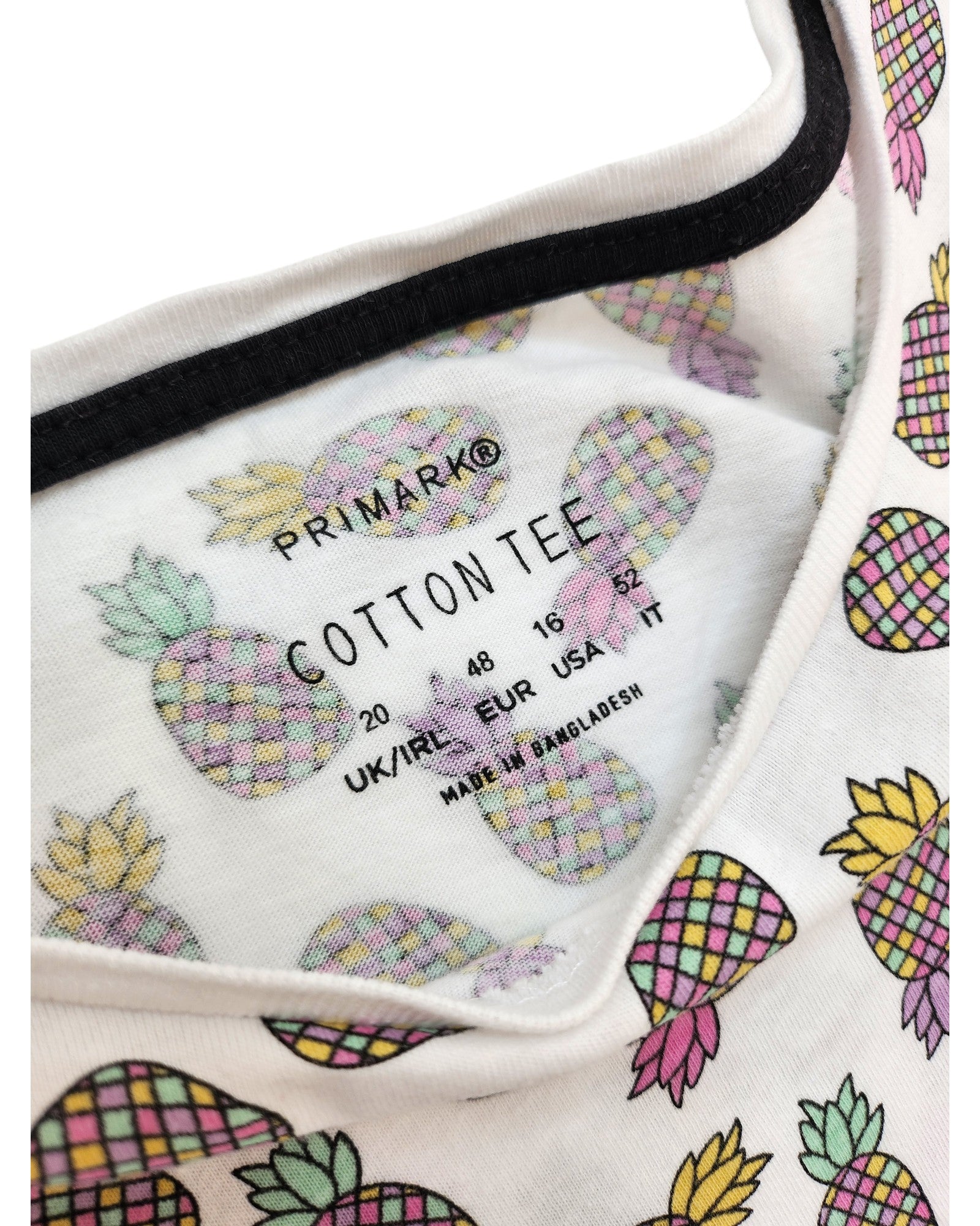 Close-up of the inside label of a Primark Upcycled Breastfeeding & Pumping Pineapple T-shirt UK20, featuring regional sizes. Made in Bangladesh, this eco-friendly piece values upcycled preloved clothing with a fun pineapple print.