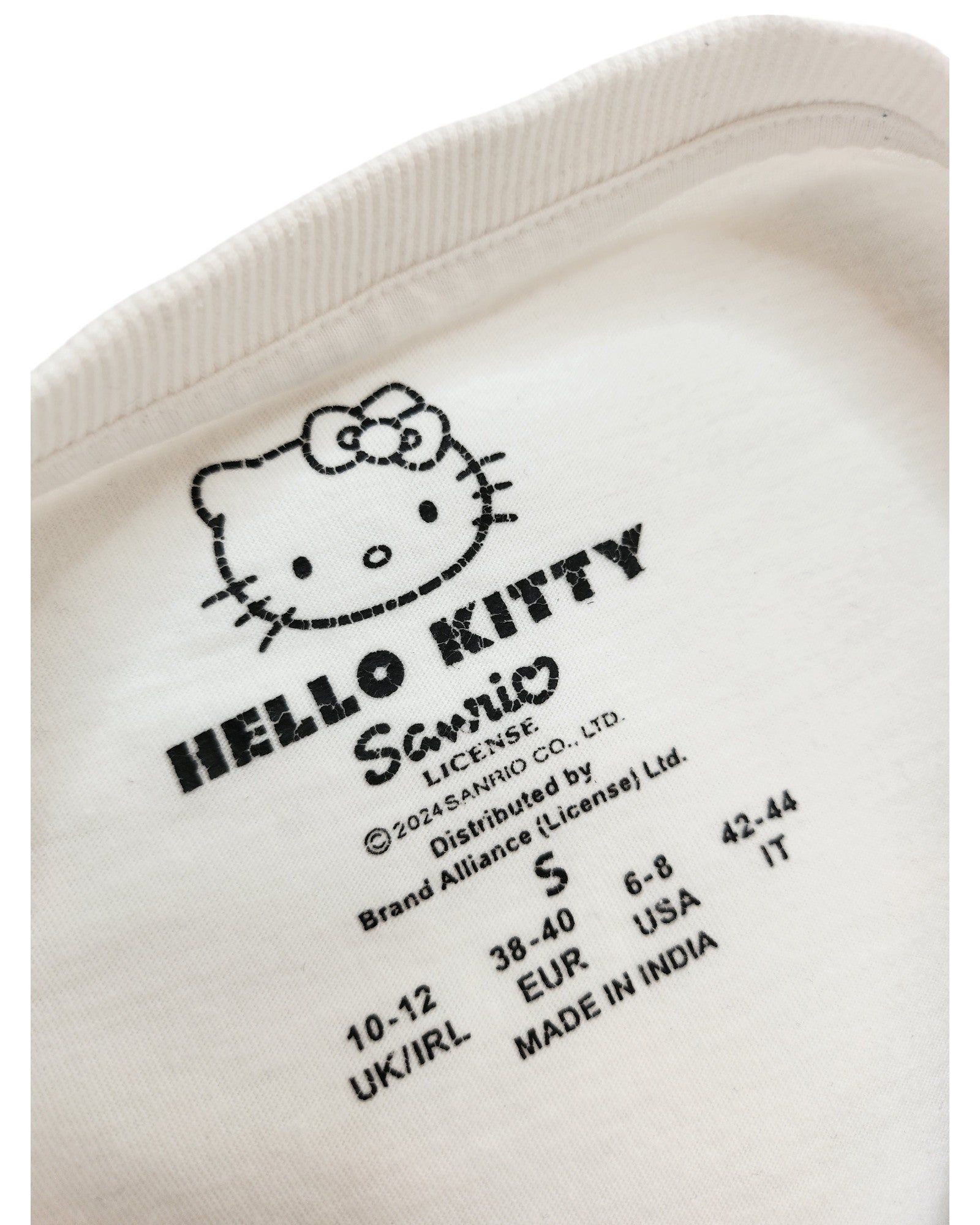 Close-up of a white Primark clothing label on an Upcycled Breastfeeding & Pumping Hello Kitty t-shirt (S/UK10/12), showing the character, logo, regional sizing, and Made in India—ideal for fans of upcycled apparel.