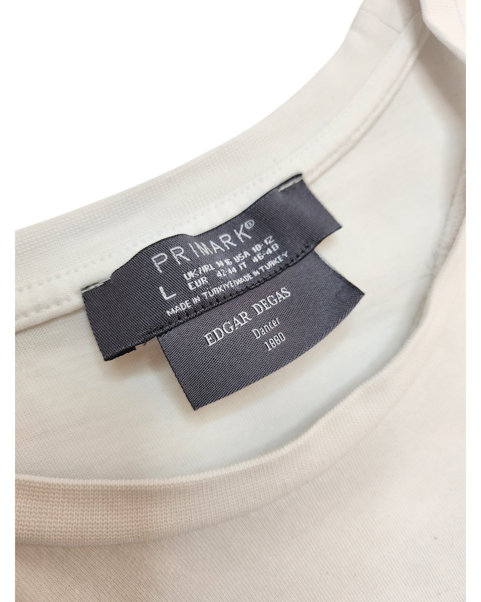 Close-up of a white Upcycled Breastfeeding & Pumping Ballet Art T-shirt (L, UK14/16) by Primark. Two black labels: top shows Primark branding and size; lower label reads EDGAR DEGAS, Dancer, 1880—highlighting eco-friendly fashion.