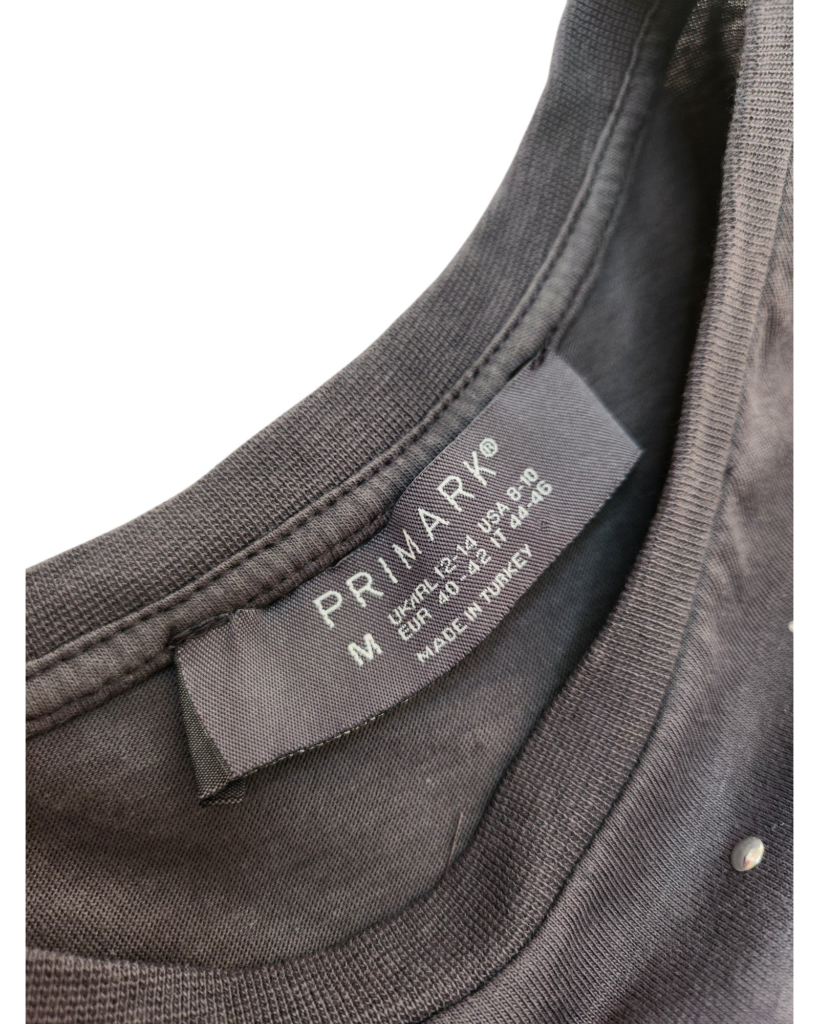 Close-up of a black Primark fabric label on the Upcycled Breastfeeding & Pumping Grey Festival Fringe T-shirt, size M (UK 12/14)—a stylish, eco-friendly choice for nursing mothers. Made in Turkey.