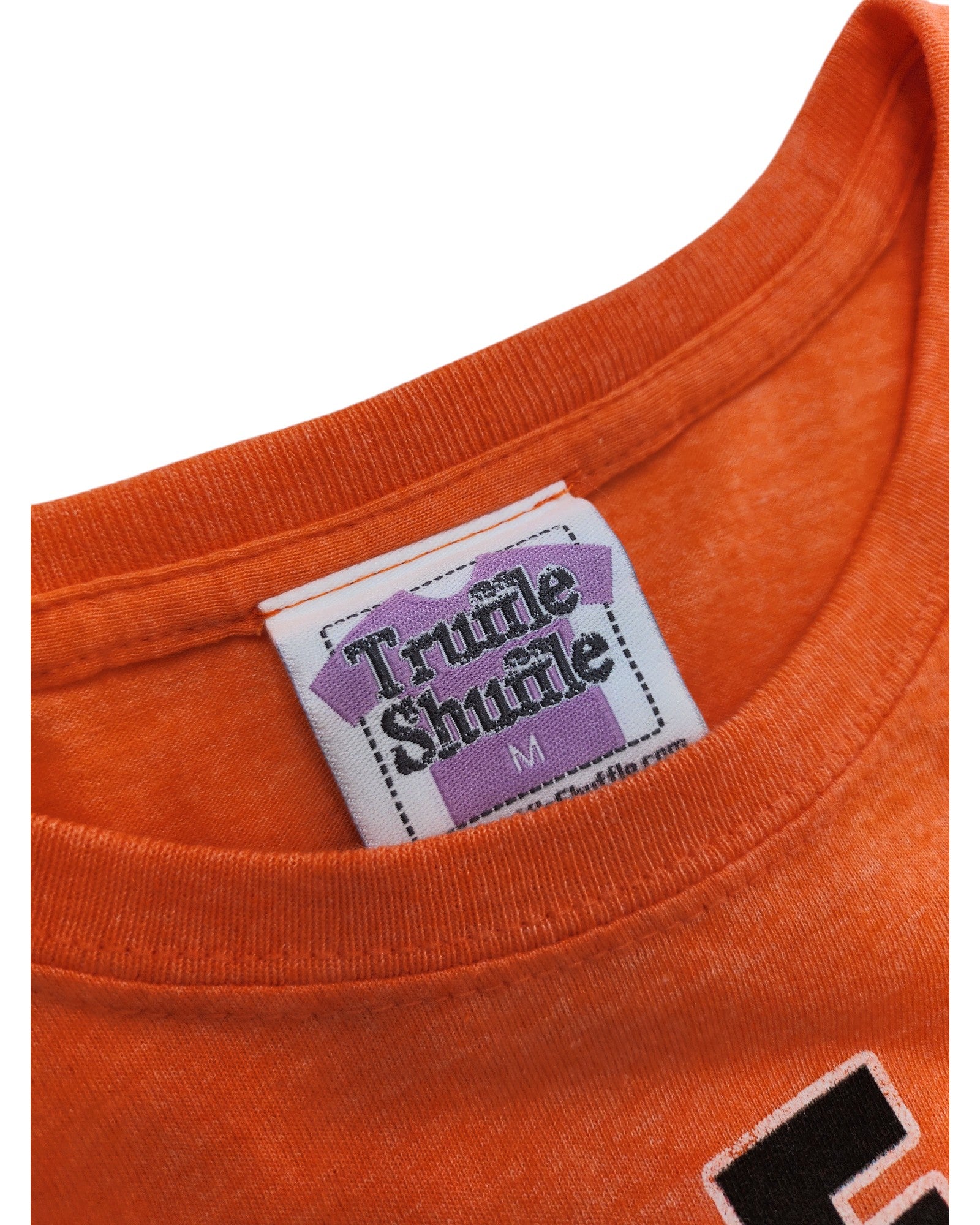 Close-up of the neckline of an orange Upcycled Breastfeeding & Pumping Little Miss Busy t-shirt M with a Truffle Shuffle tag in black on a white and purple label, highlighting the brand’s commitment to eco-friendly fashion.