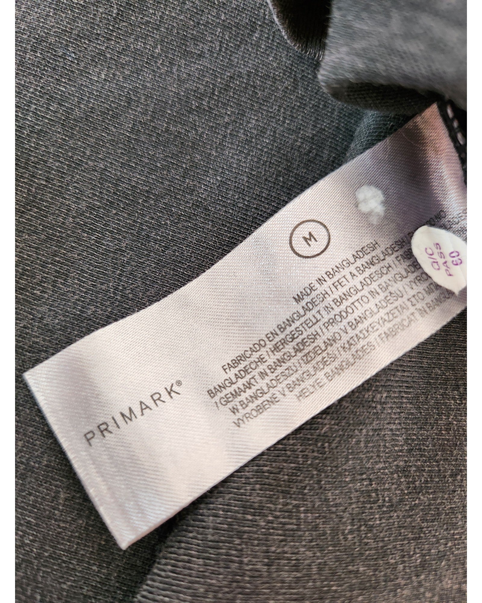 A close-up of a Primark label on an upcycled preloved Rolling Stones Voodoo nursing & pumping t-shirt, size M, featuring care instructions and indicating its made in Bangladesh.