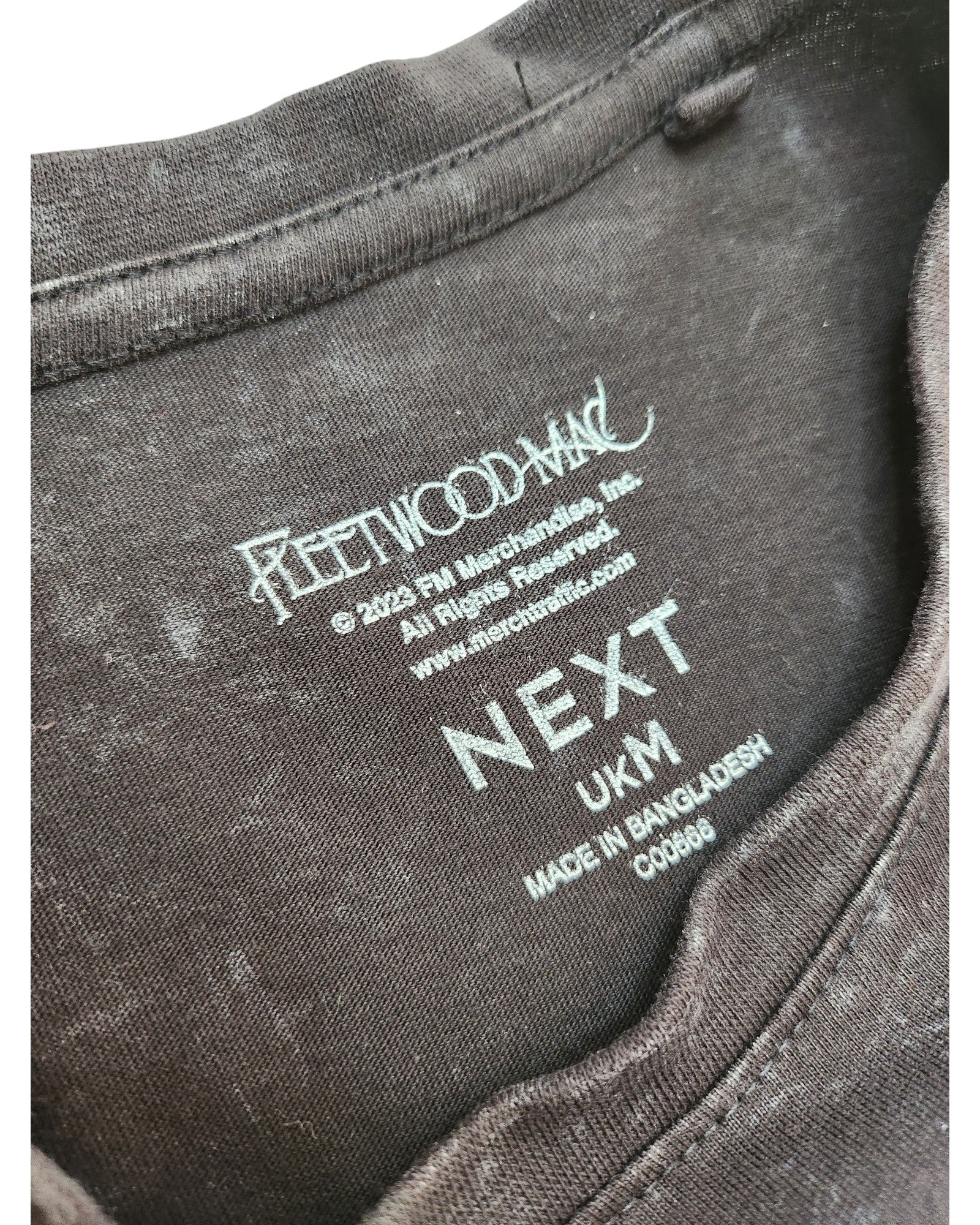 Close-up of a brown NEXT upcycled breastfeeding & pumping rainbow Fleetwood Mac t-shirt (size M), highlighting preloved fashion details and manufacturing info on the printed collar label.