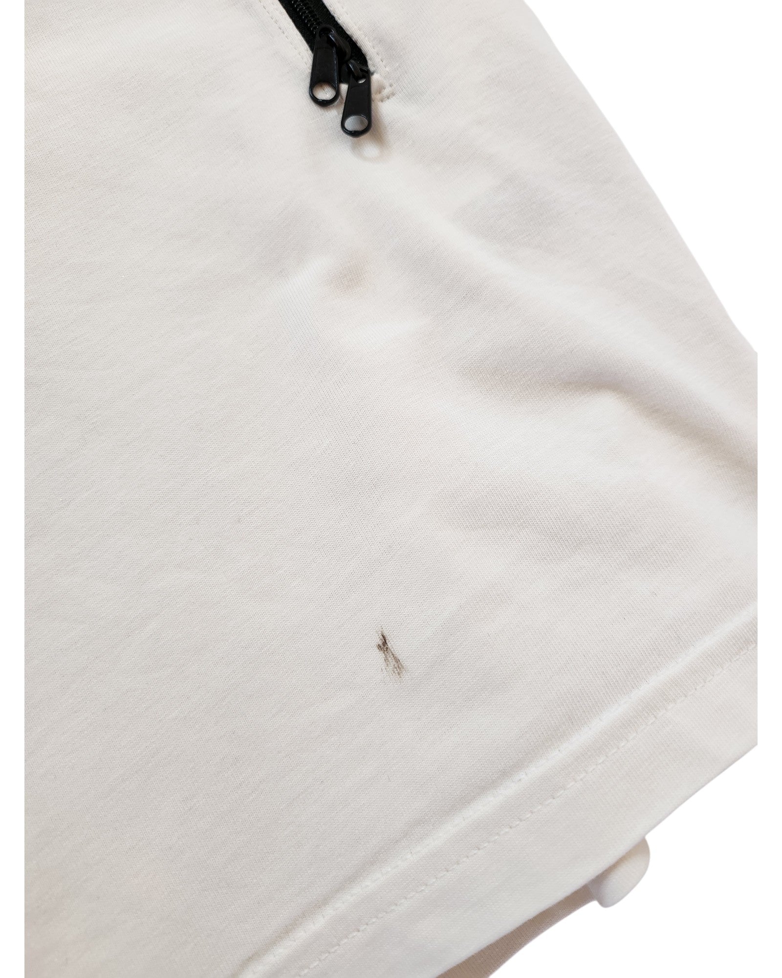 A close-up of a white H&M Upcycled Breastfeeding & Pumping The Rolling Stones t-shirt (XL, cream/red) shows a small thin black stain near the bottom hem and a black zipper at the top.