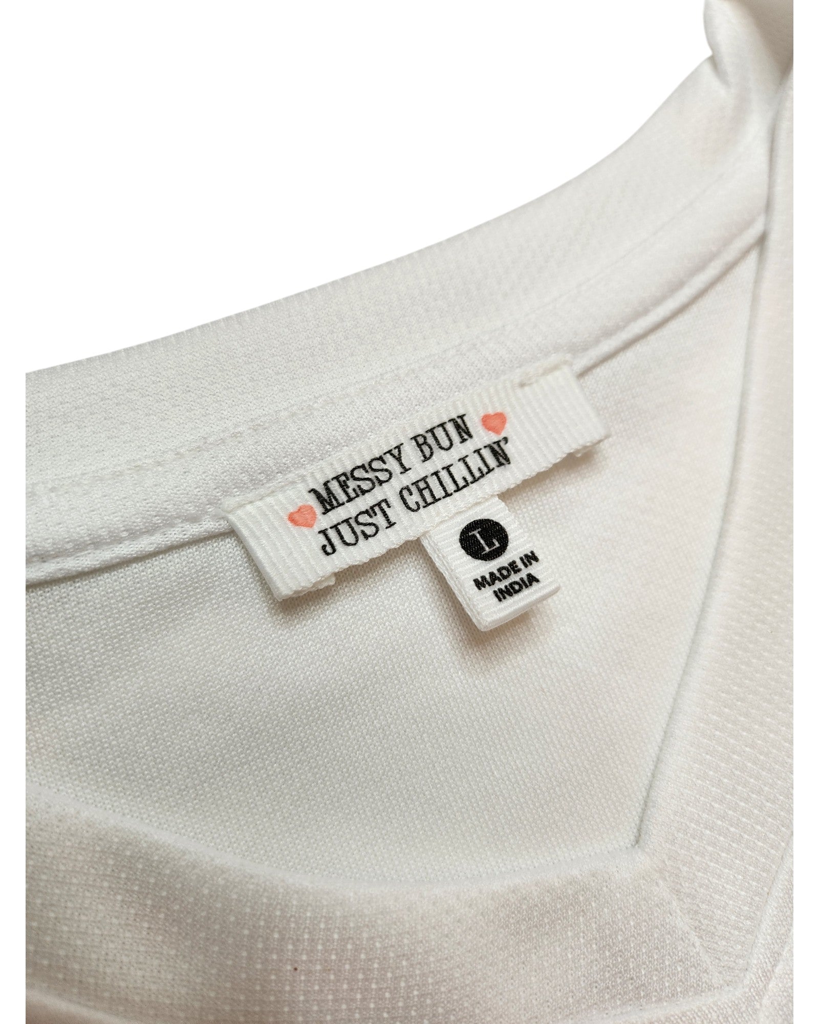Close-up of a white Upcycled Breastfeeding & Pumping 89 Swiftie Football Jersey t-shirt (L) from Messy Bun Just Chillin, showing two tags—one with brand and pink hearts, and one labeled L MADE IN INDIA. A fresh take on preloved fashion.