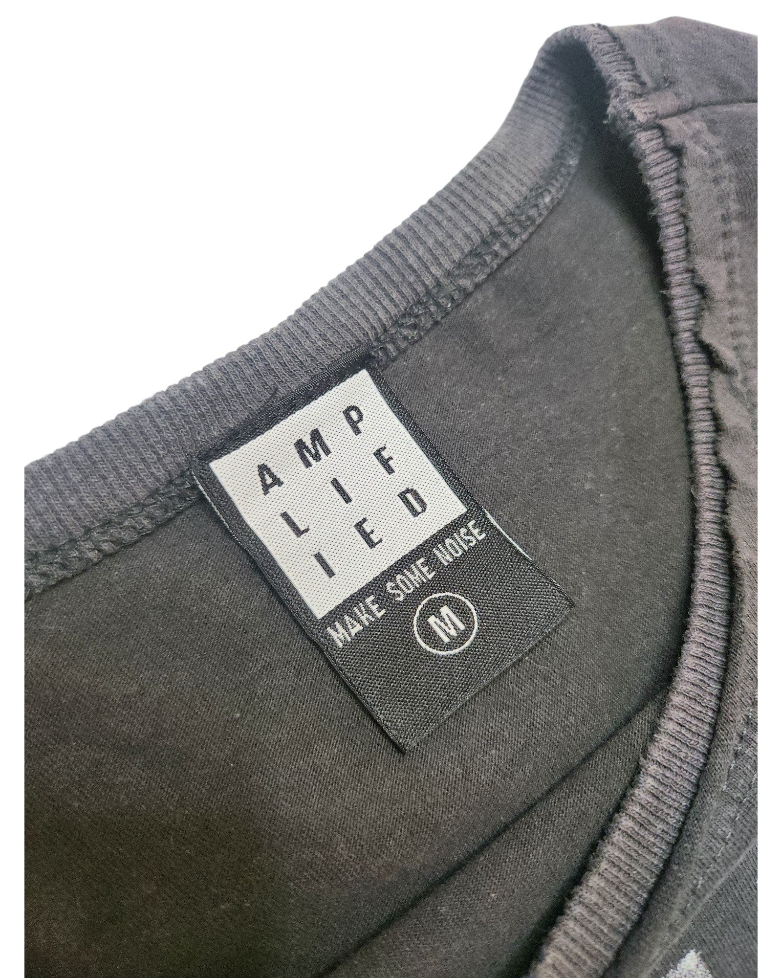 Close-up of a black Amplified label on an upcycled Metallica Guitar Band breastfeeding & pumping t-shirt (M), reading AMPLIFIED and MAKE SOME NOISE with a circled M for medium. The eco-friendly neckline is also shown.