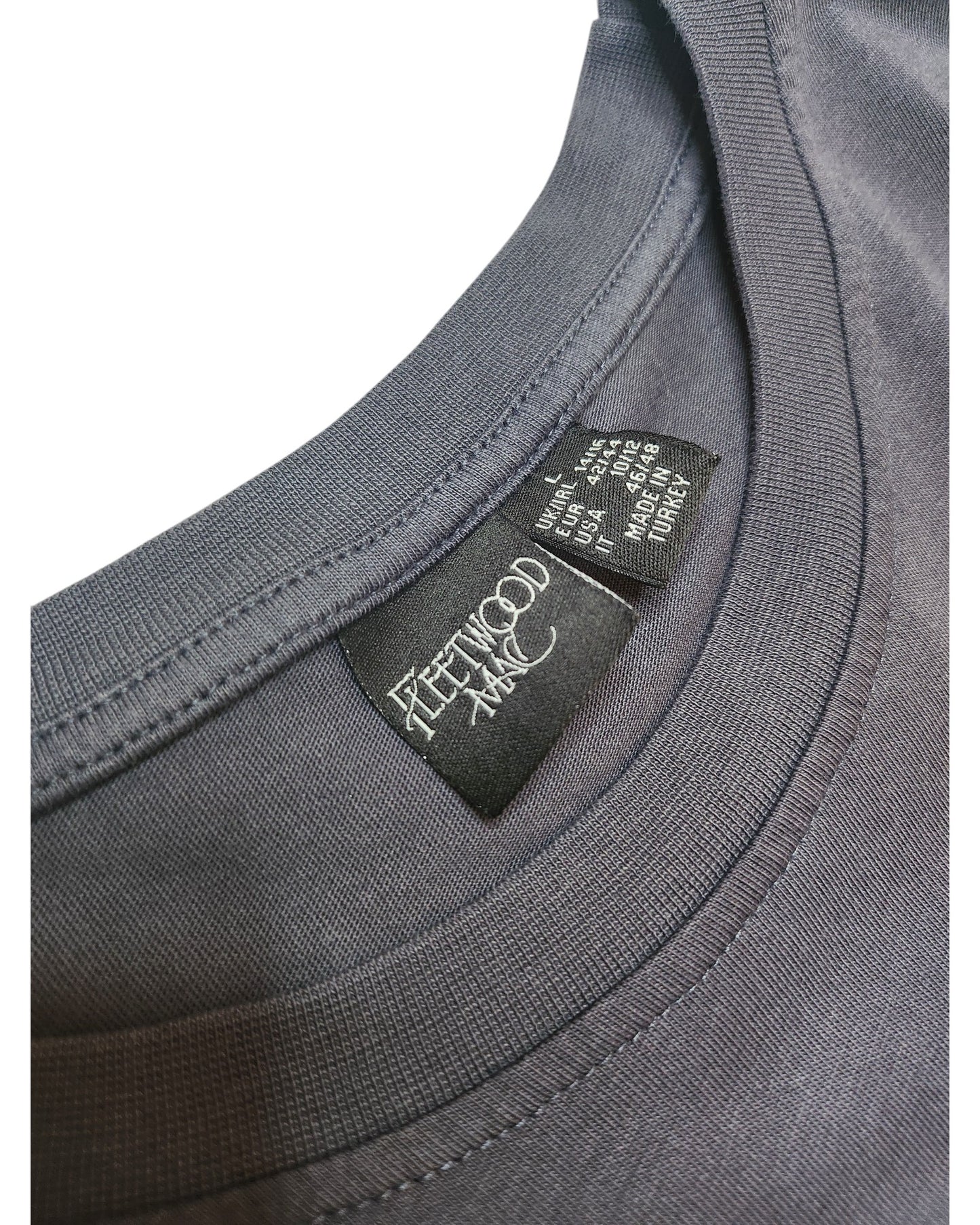 Close-up of a gray upcycled Primark t-shirt (size L UK14/16) for breastfeeding and pumping, featuring a black inner collar tag with FLEETWOOD MAC in white text and care instructions in smaller white font.
