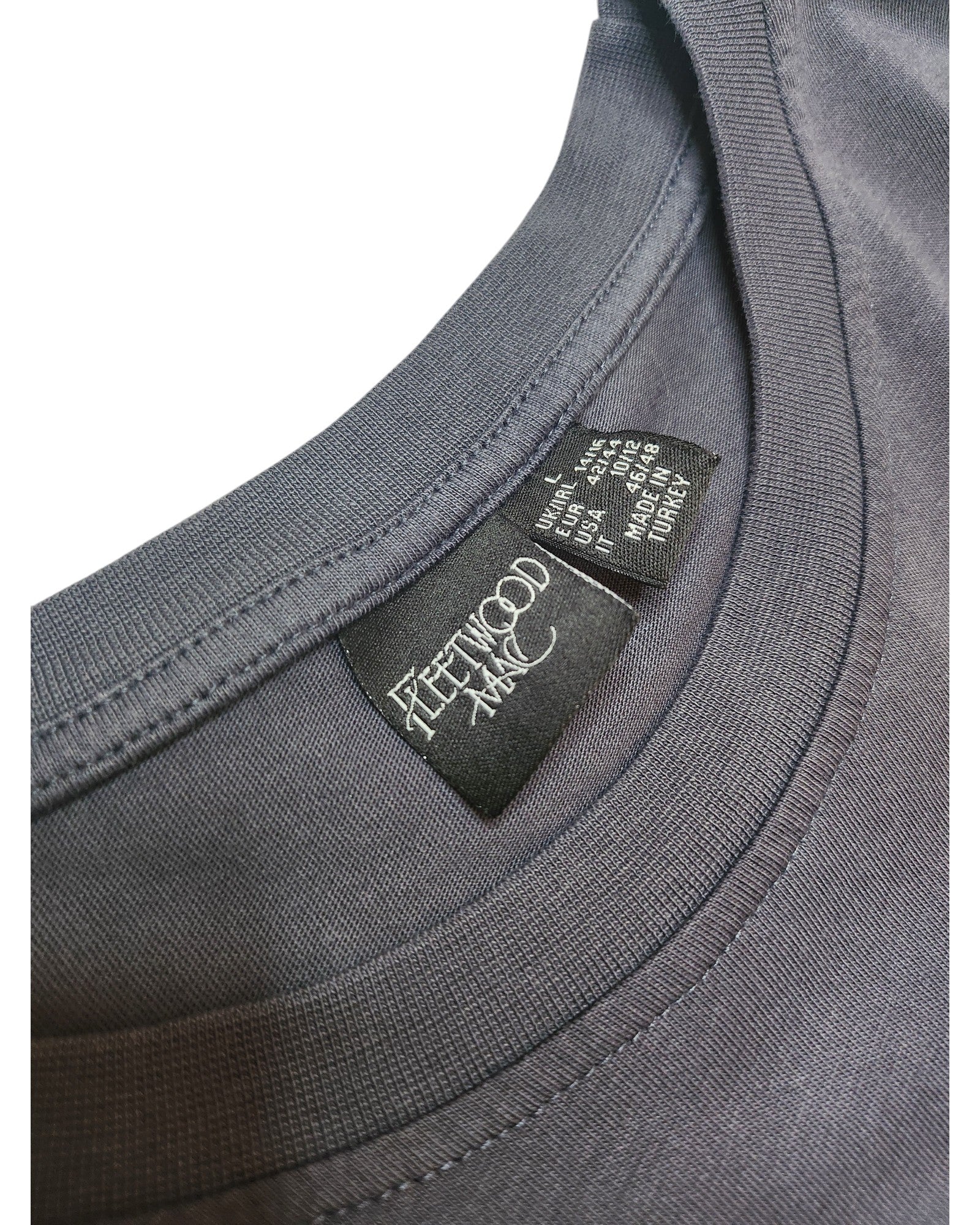 Close-up of a gray upcycled Primark t-shirt (size L UK14/16) for breastfeeding and pumping, featuring a black inner collar tag with FLEETWOOD MAC in white text and care instructions in smaller white font.